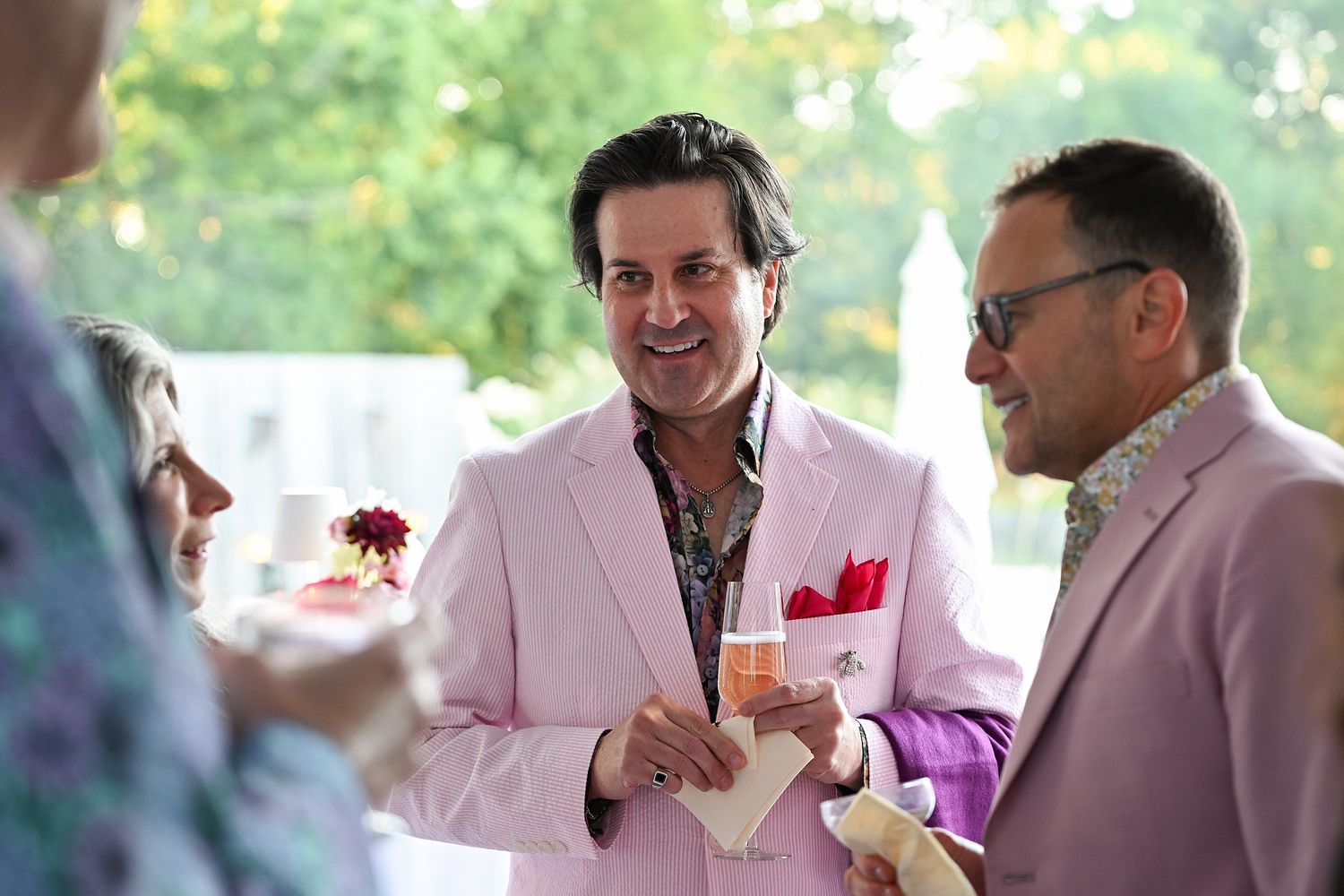 Two people in pink and light colored suits having a conversation at an outdoor social gathering.