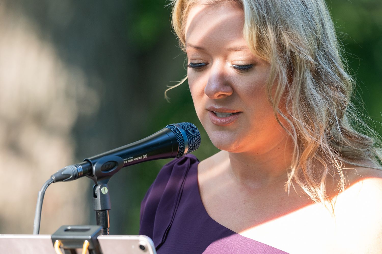 Person in purple shirt performs music outdoors while playing acoustic guitar in natural setting.