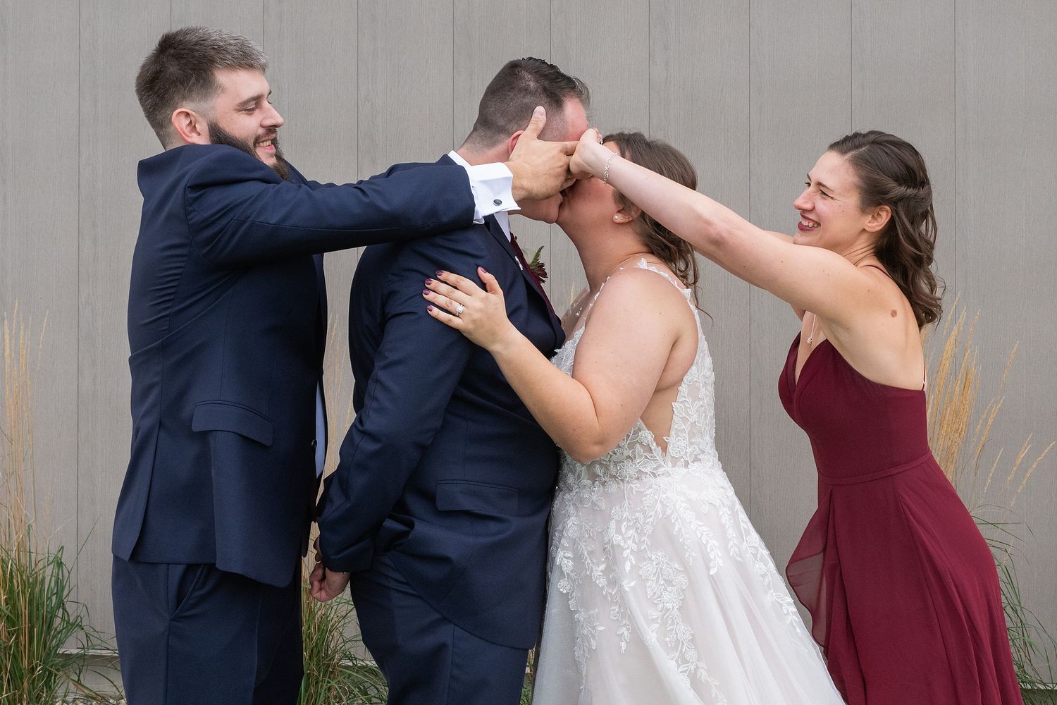 Wedding party playfully helping bride and groom share their first kiss.