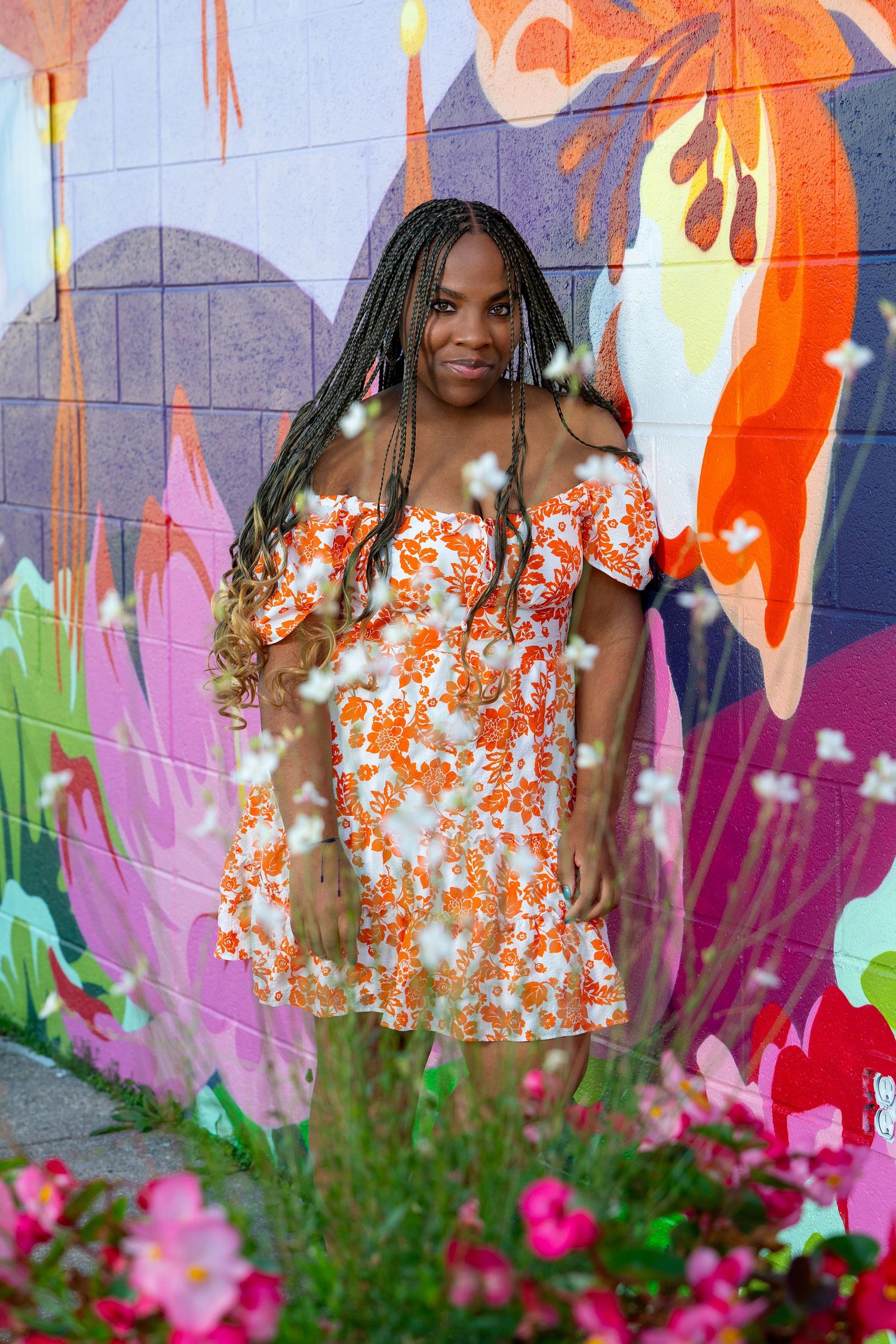 A colorful photoshoot against a vibrant mural wall with orange and pink flowers in the foreground.
