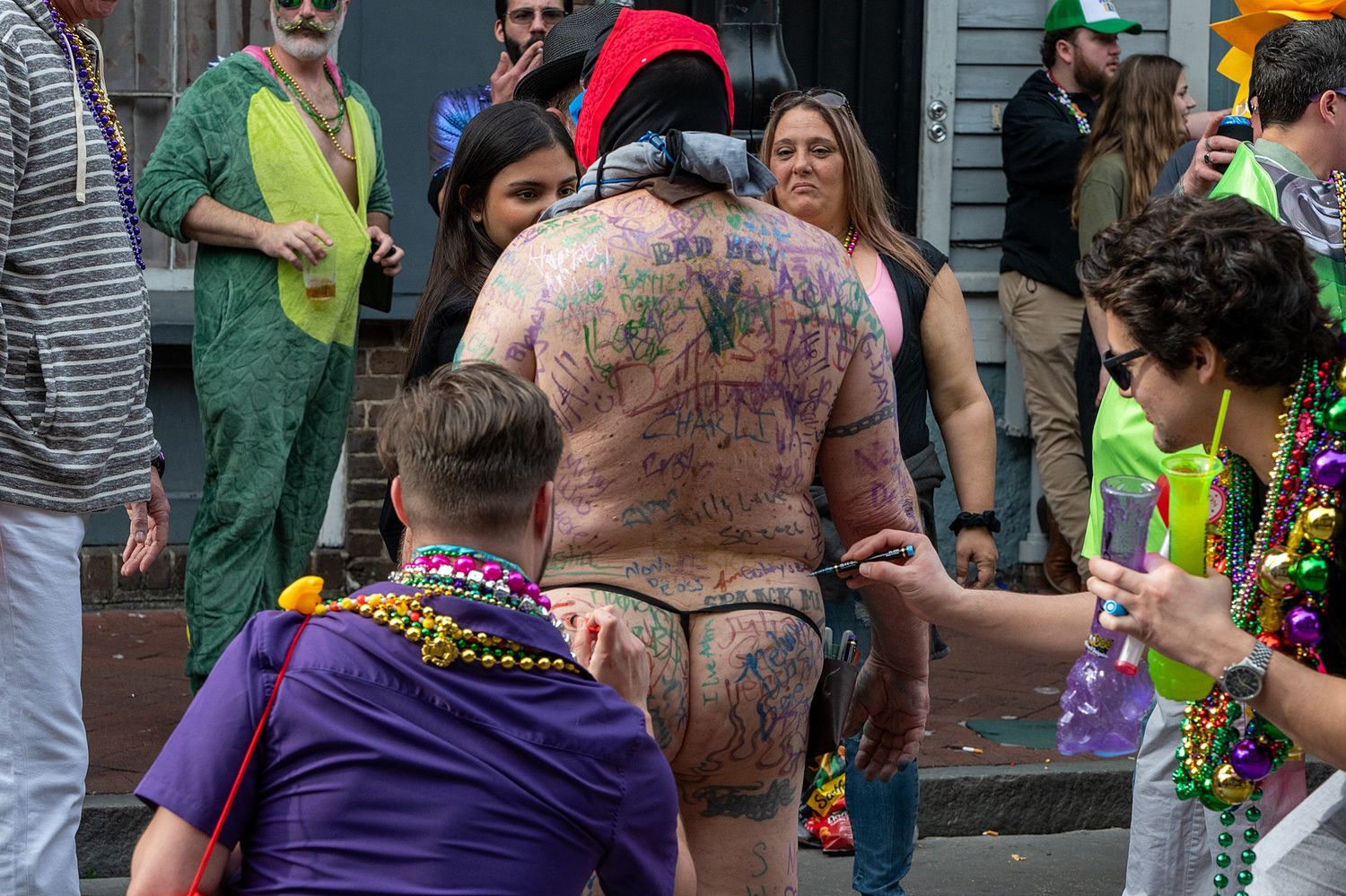 Mardi Gras revelers in purple and green attire celebrate in a crowded street.
