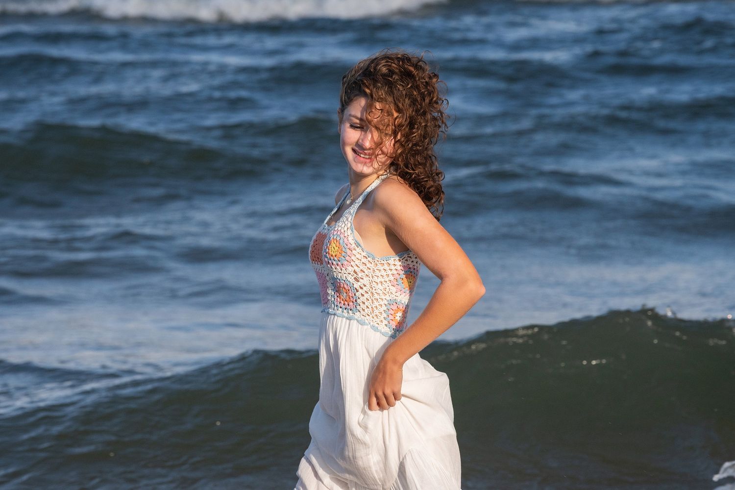 A white sundress with embroidered details stands out against the deep blue ocean waves.