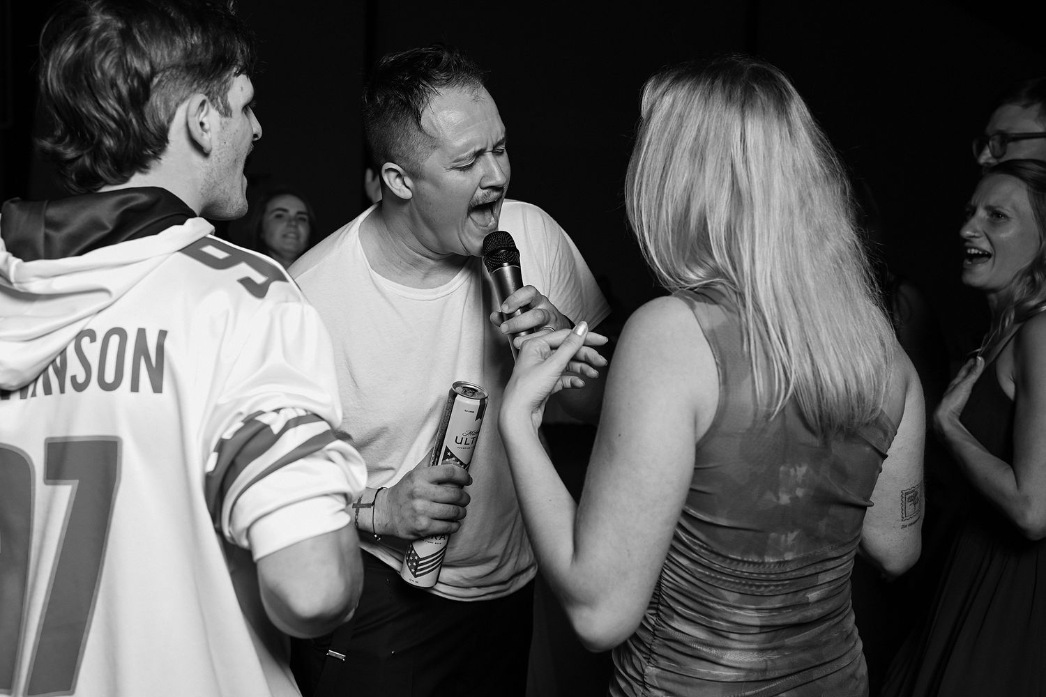 Guests sing karaoke together at a lively wedding reception party in black and white photo.