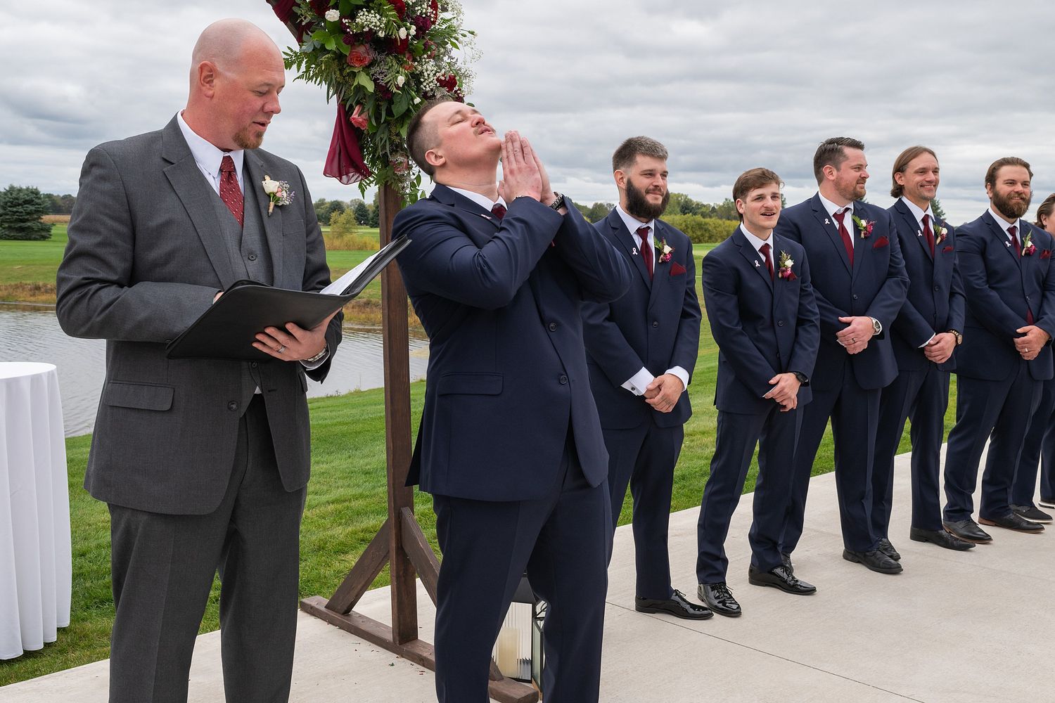 Emotional groom reacts as bride walks down aisle at outdoor waterfront wedding ceremony.