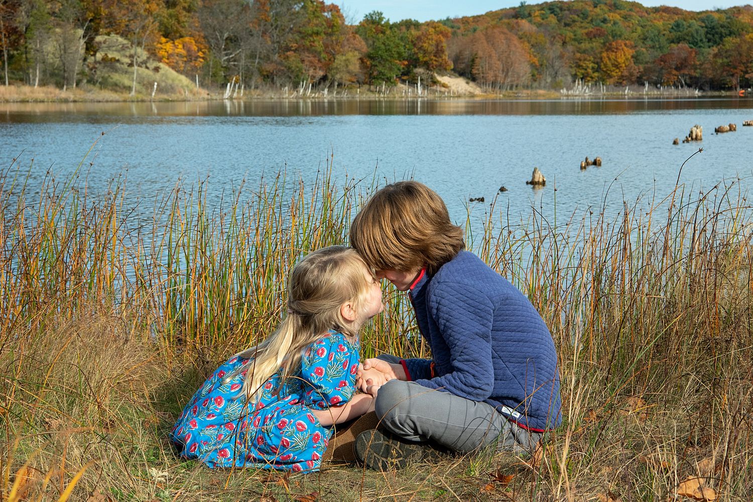 People relaxing by scenic autumn lake with fall foliage in background.