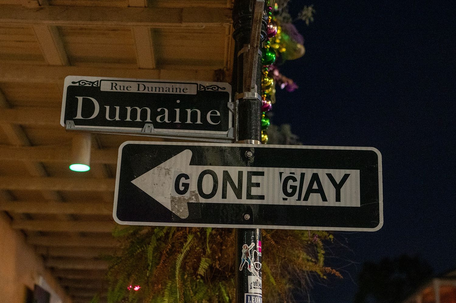 Street sign reading 'Gone Gay' with decorative lights at night in the French Quarter.