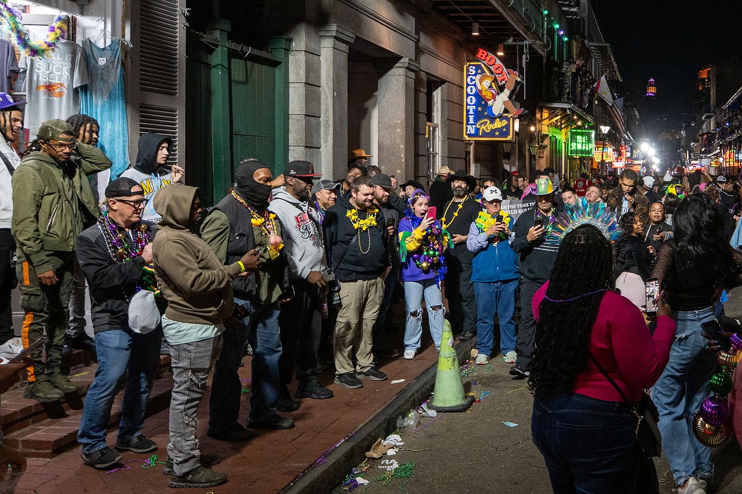 Bustling nightlife scene on Bourbon Street with crowds of people walking past historic buildings.