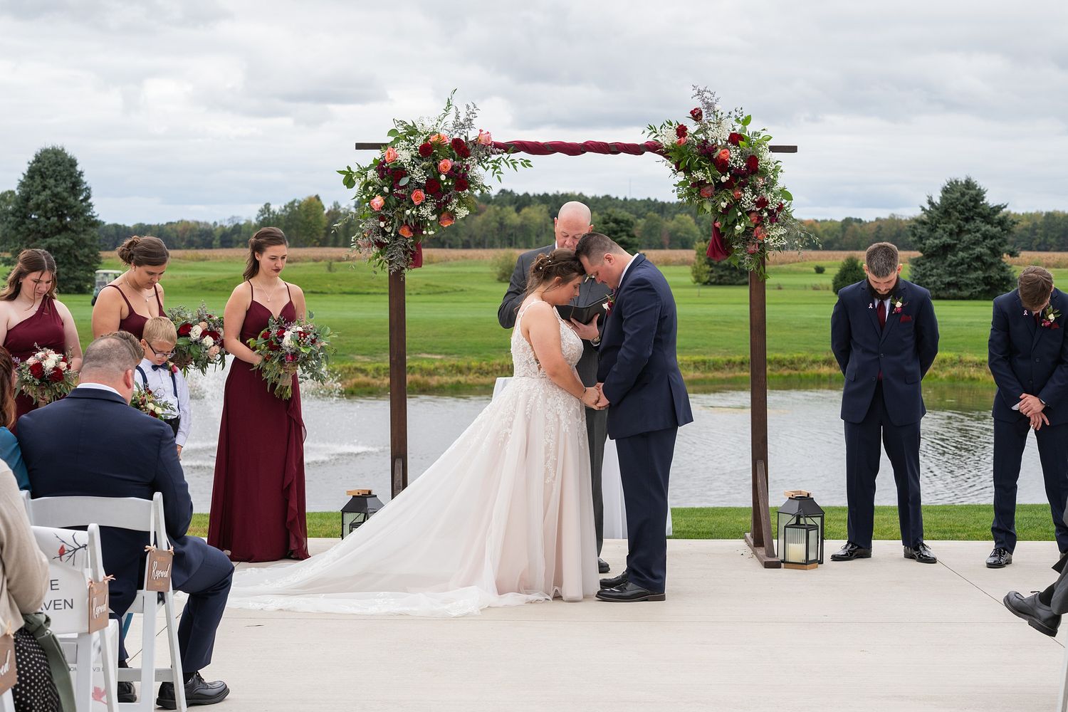 Bride and groom share first kiss under floral arch at outdoor waterfront wedding ceremony.