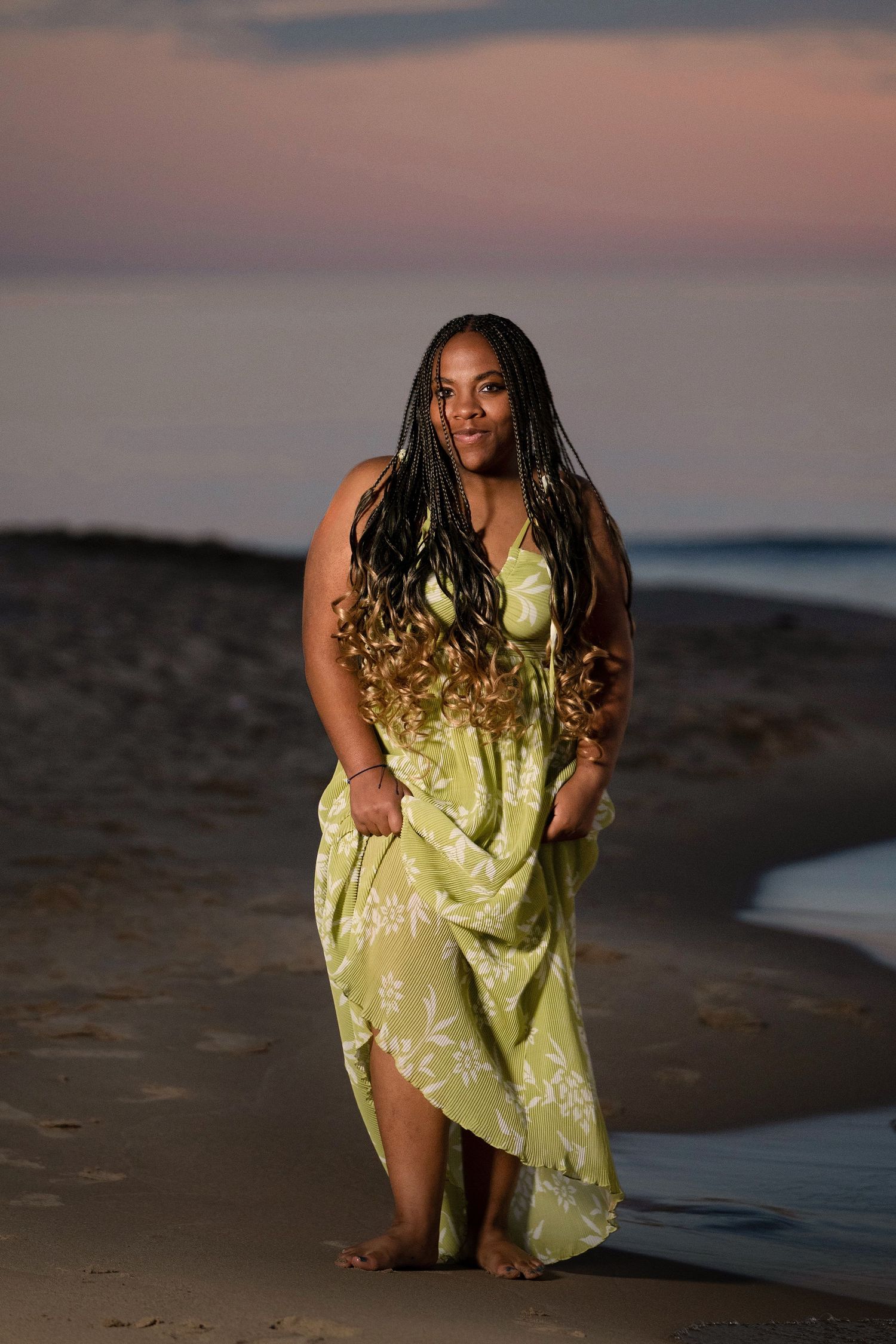 Figure in yellow floral dress poses on beach during golden hour sunset.