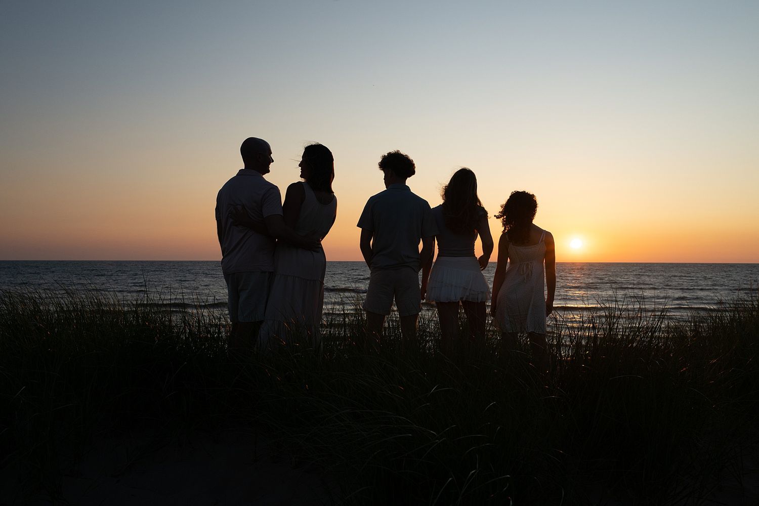 Silhouetted figures against dramatic sunset sky at beach overlook.