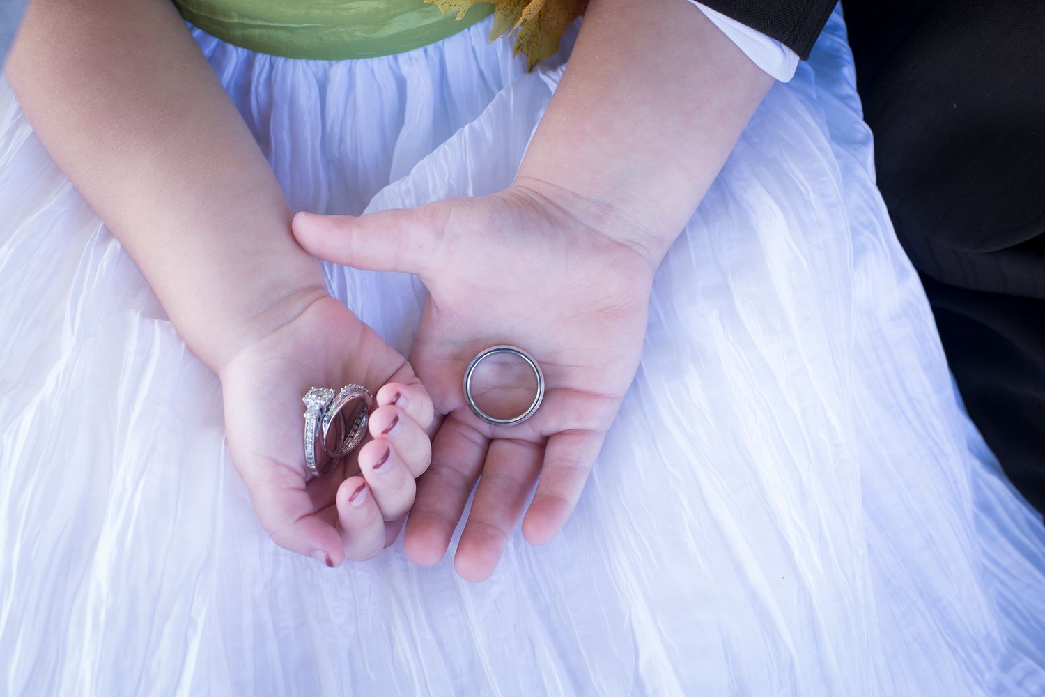 Delicate wedding rings nestled on a pink flower against tulle fabric.
