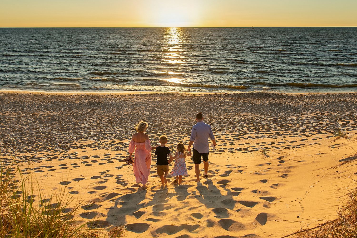 Silhouettes walking along beach at sunset with golden light reflecting on water.