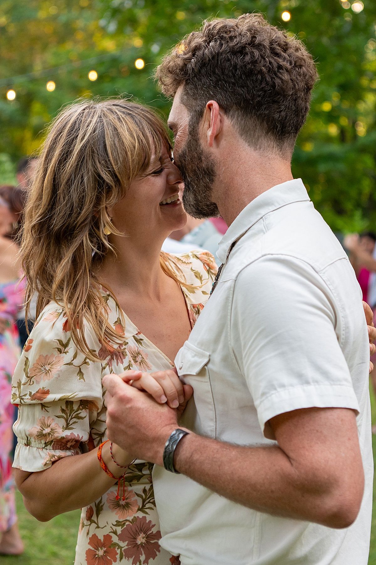 Couple dancing together outdoors with string lights in the background.