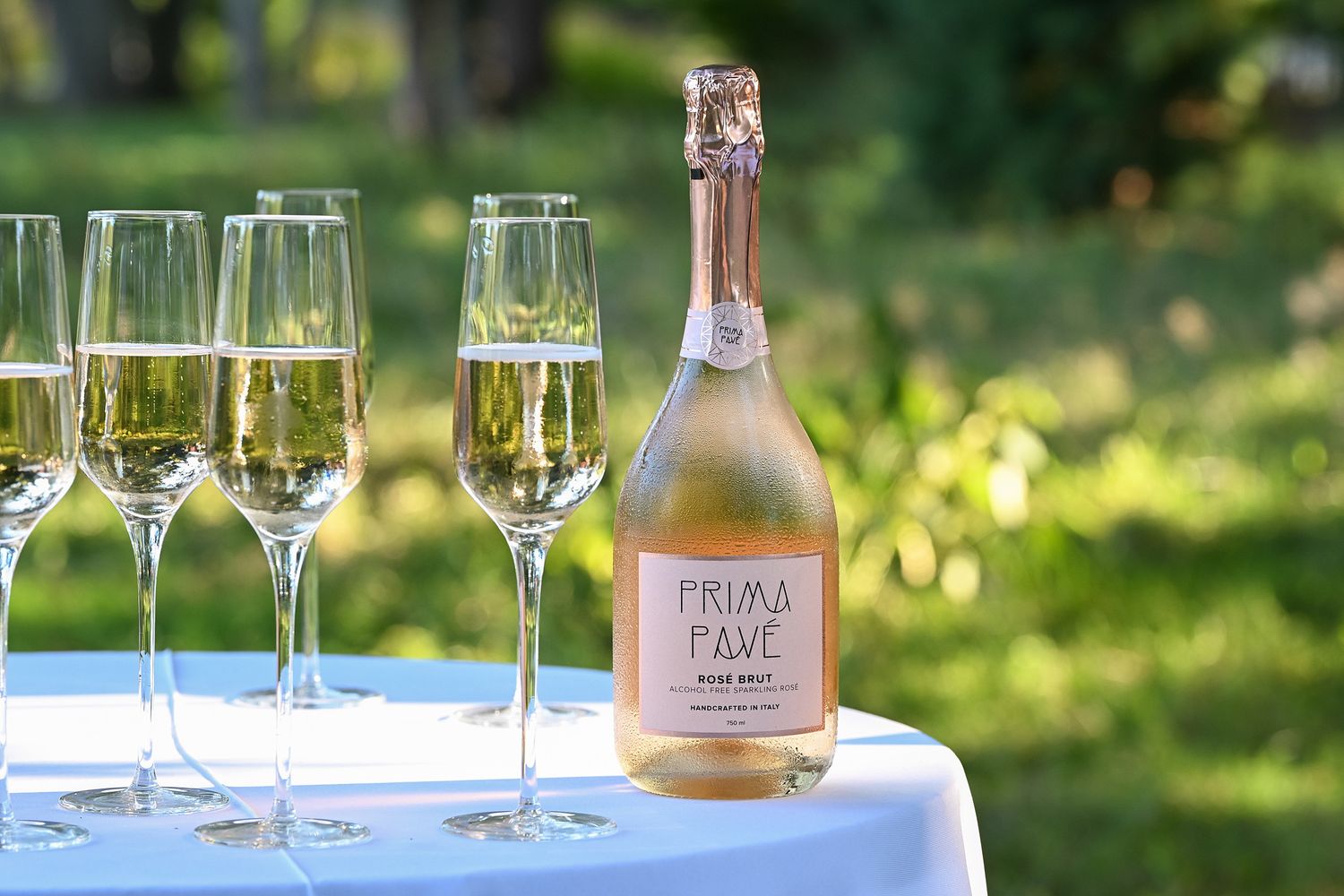 Champagne glasses and bottles arranged on an outdoor table setting with natural greenery in the background.