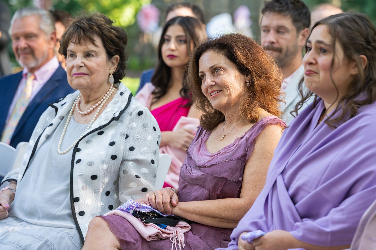 A group of people sitting together outdoors at an event wearing casual attire and watching with interest.