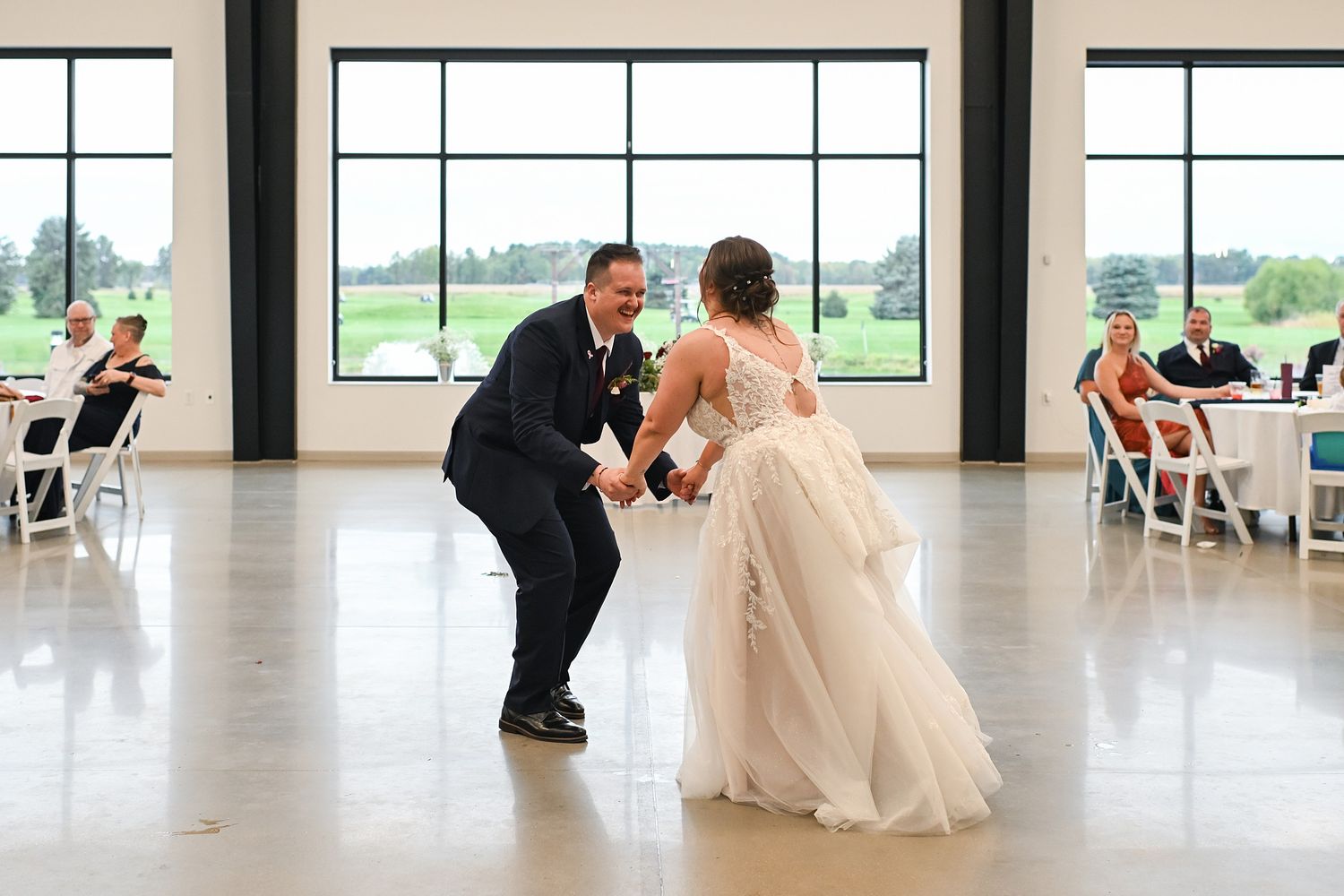 Bride and groom sharing a fun first dance in elegant modern wedding venue with large windows.