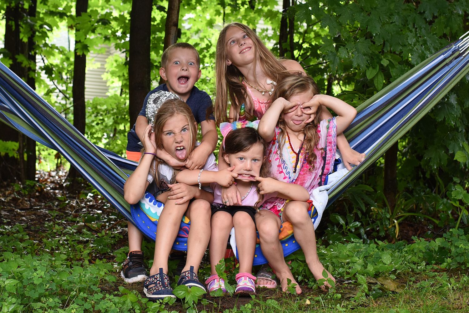 A group lounges together in a striped hammock under green summer trees.
