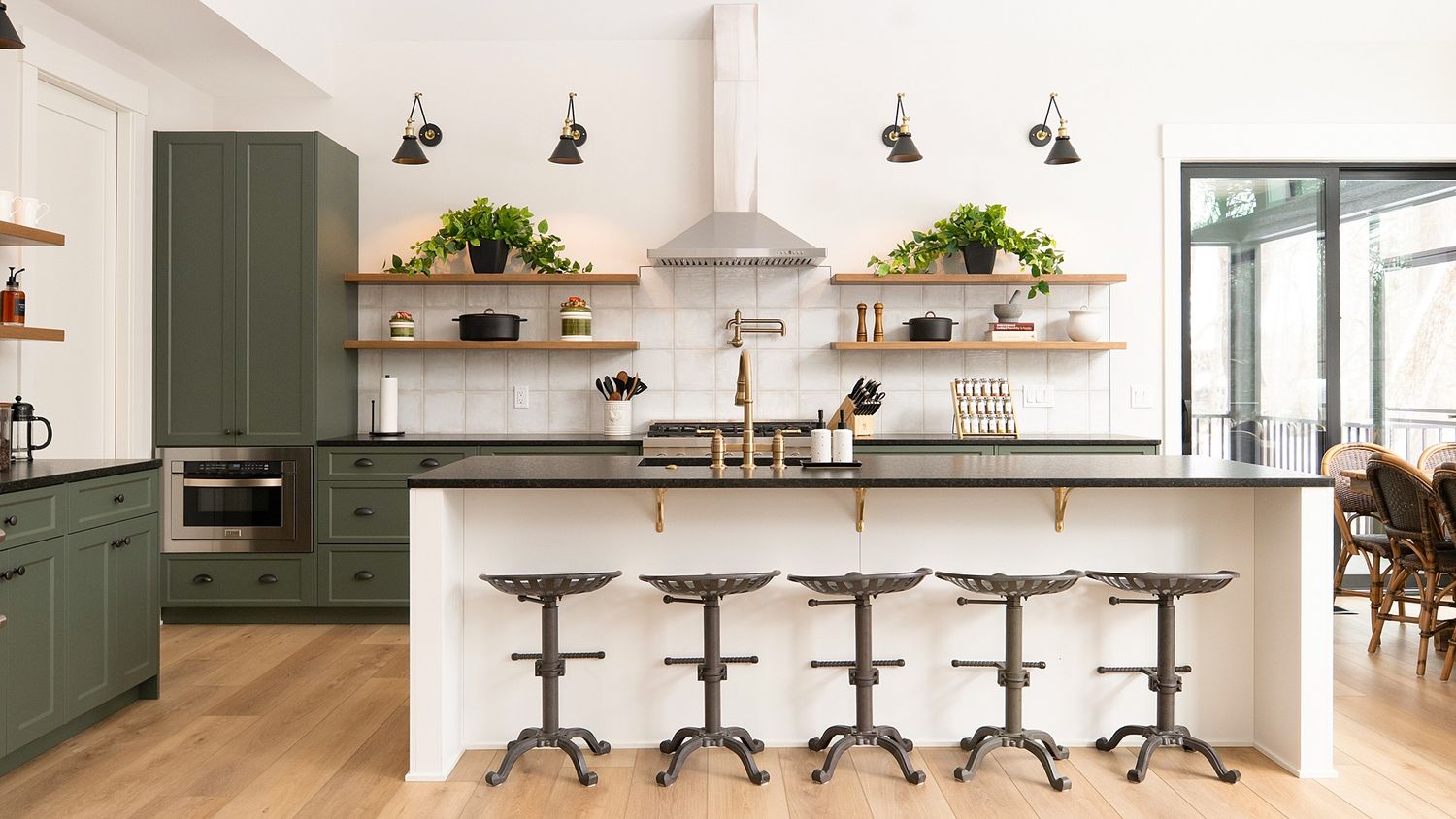 Modern white kitchen with dark green cabinets, bar seating, and pendant lighting.