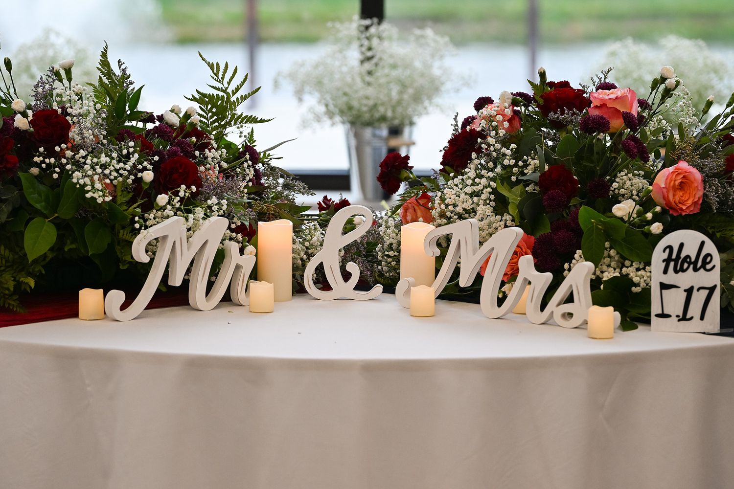 Mr. and Mrs. wooden signs with candles and red floral arrangements on wedding sweetheart table.