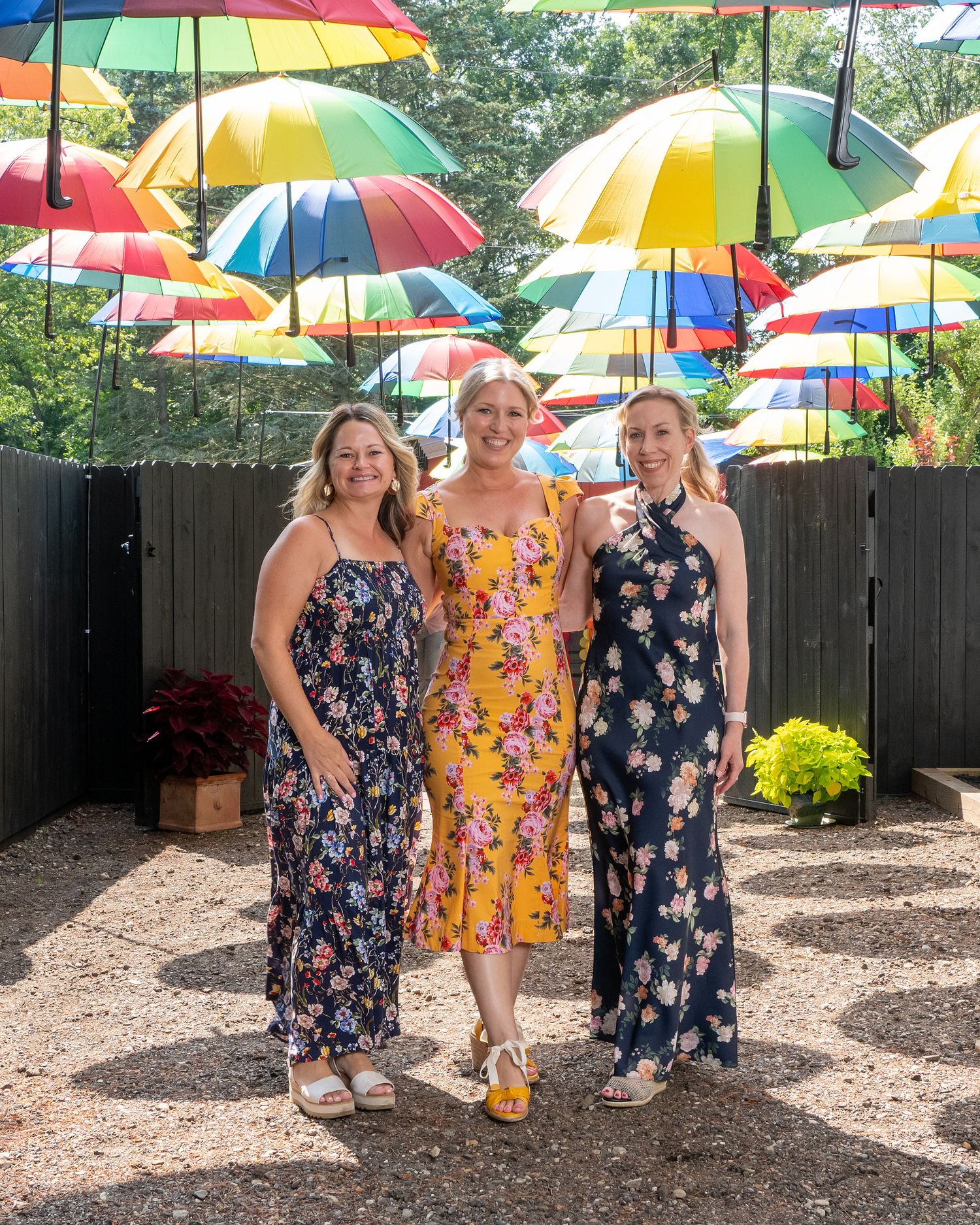 Colorful rainbow umbrellas create a vibrant canopy over a backyard gathering space on a sunny day.