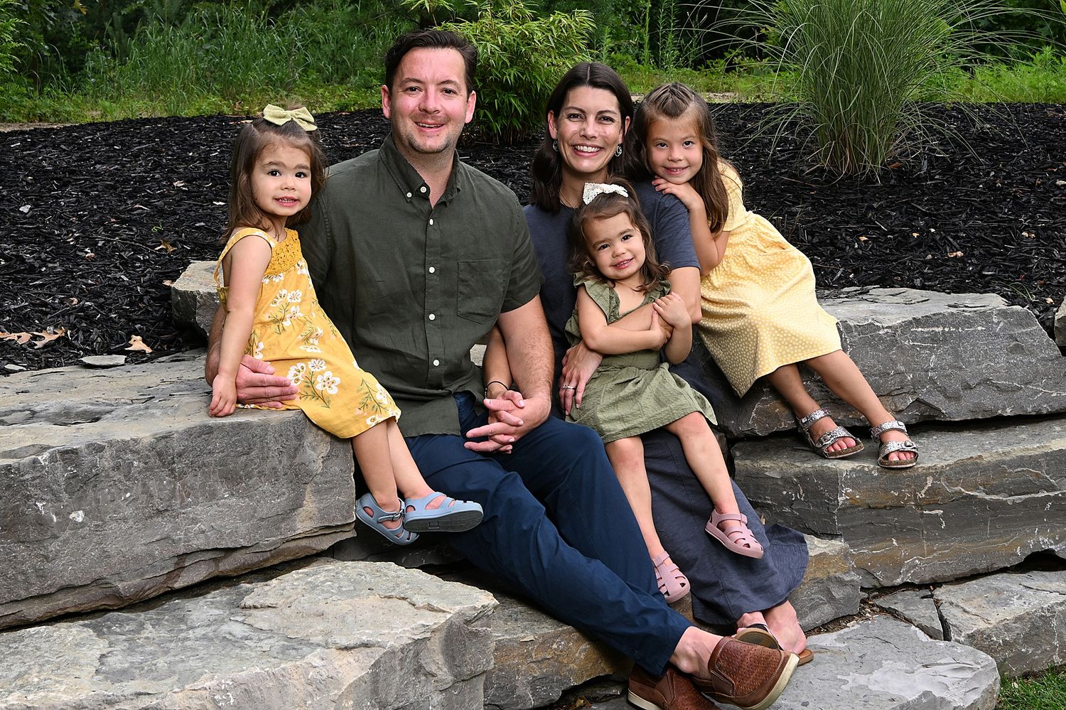 Family sitting together on dark stone steps surrounded by greenery.