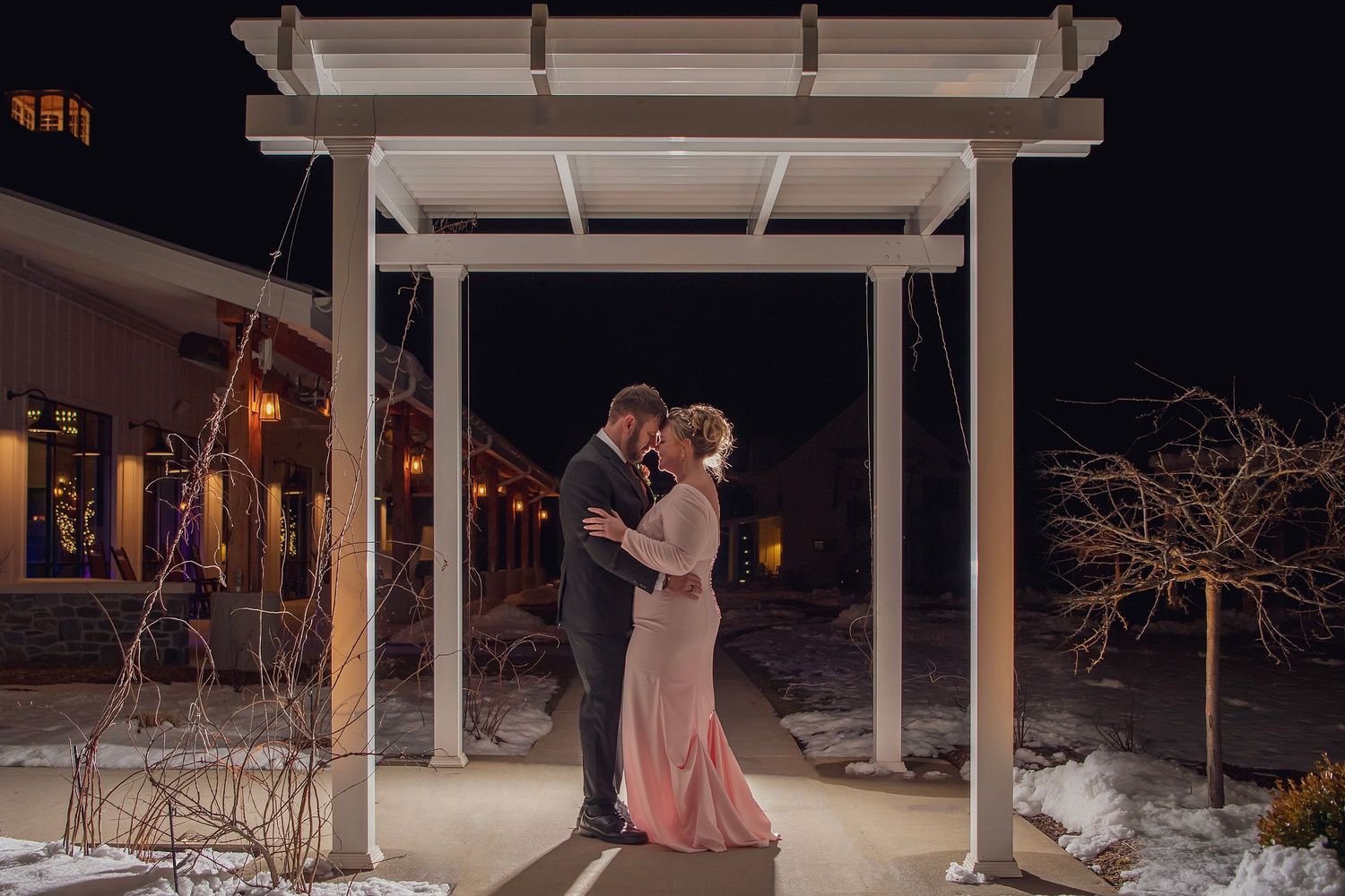 A romantic evening moment under a white pergola with string lights creating an intimate atmosphere.
