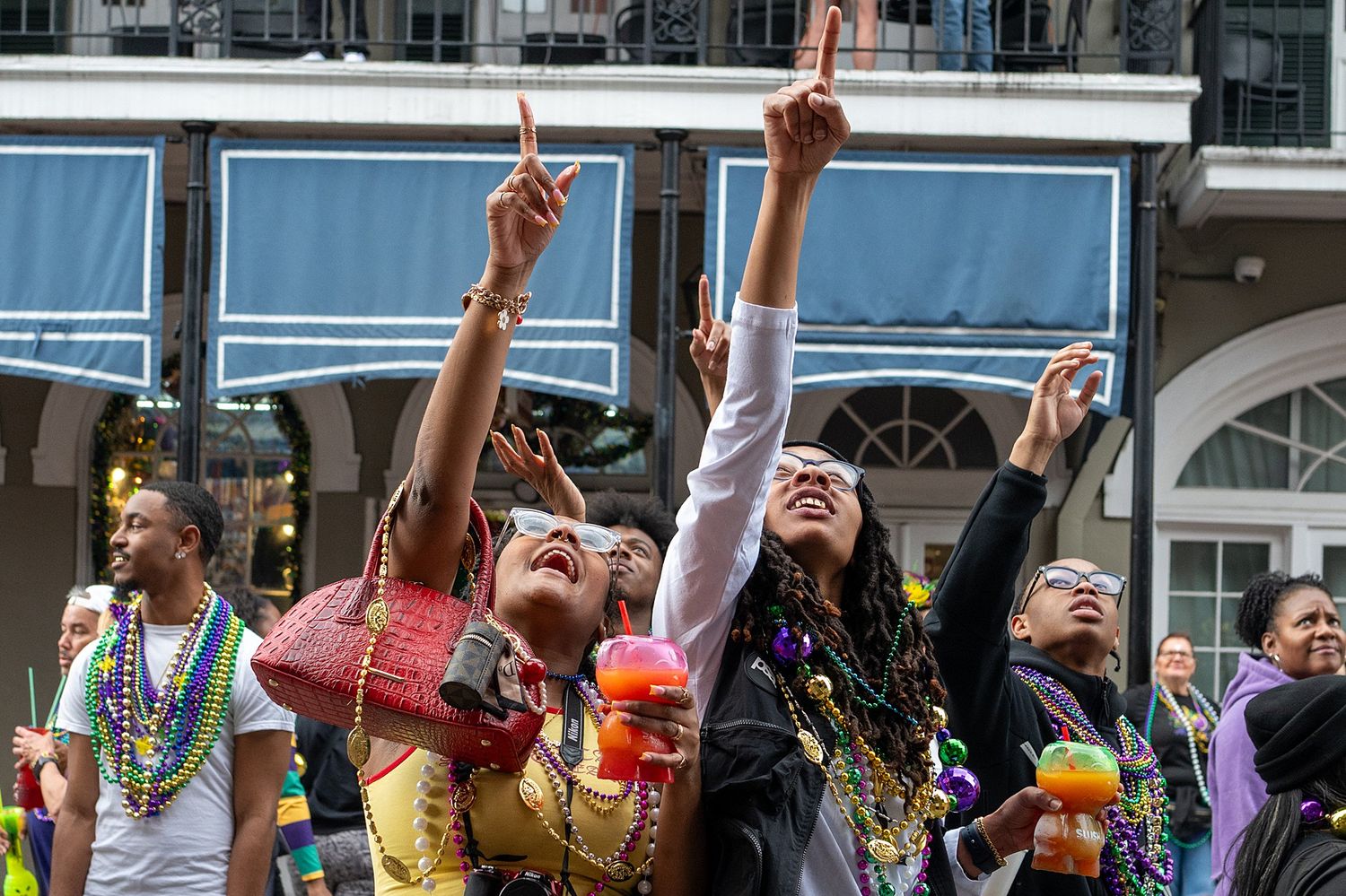 Excited crowd celebrating beneath balconies during New Orleans Mardi Gras festivities.