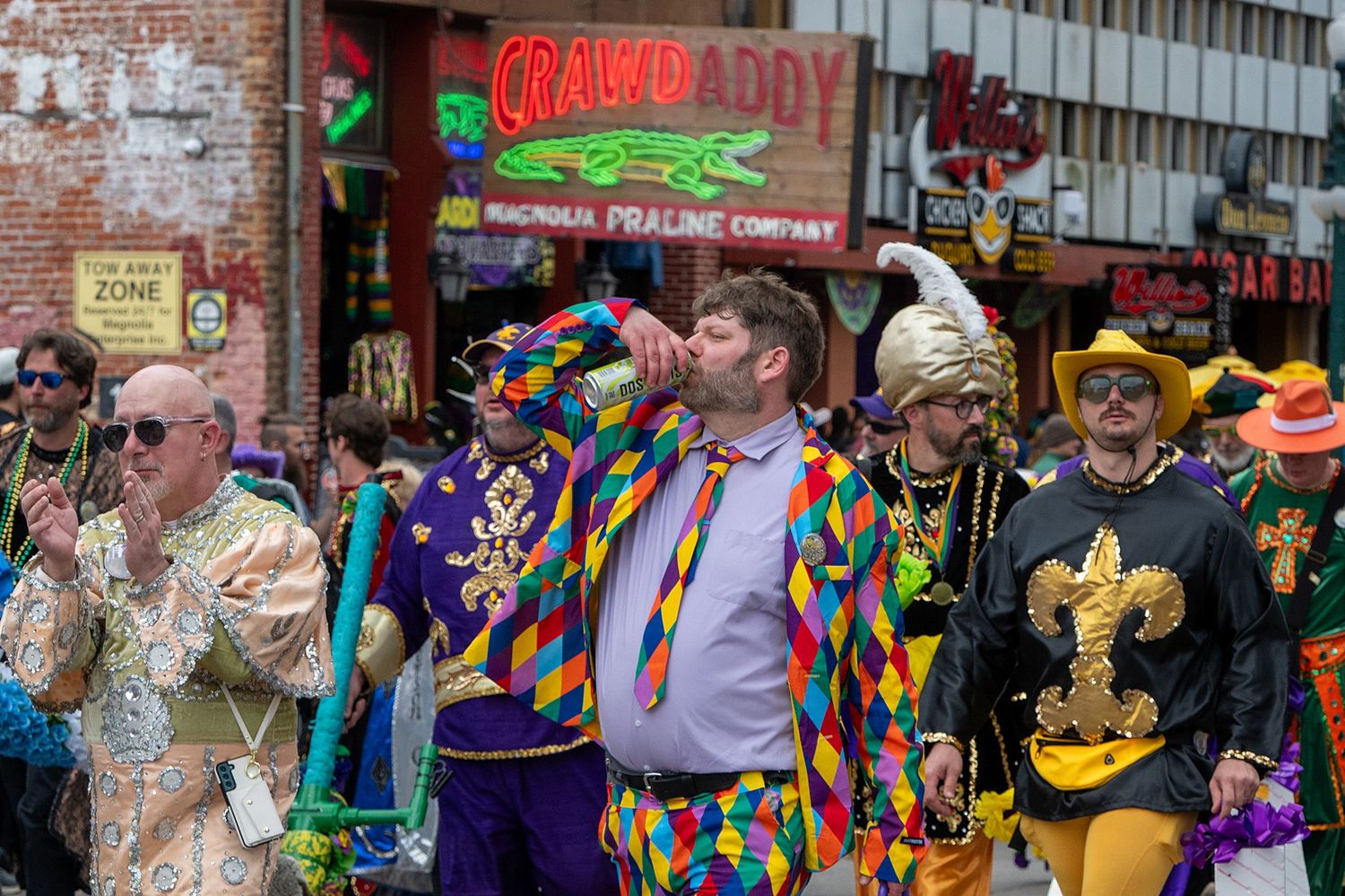 Street parade with performers in multicolored jester costumes and traditional Mardi Gras attire.