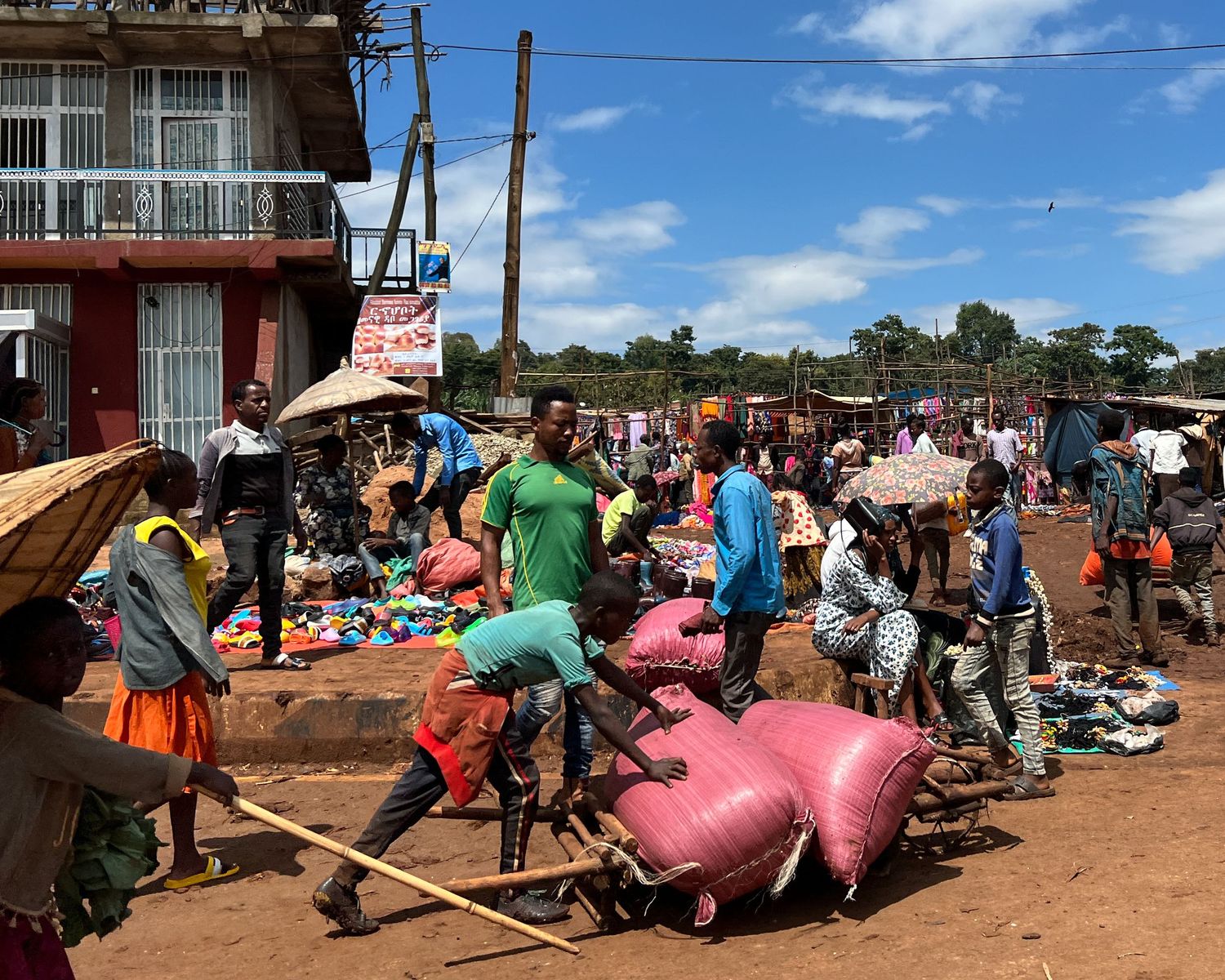 Crowded marketplace scene with people carrying pink bags and goods.