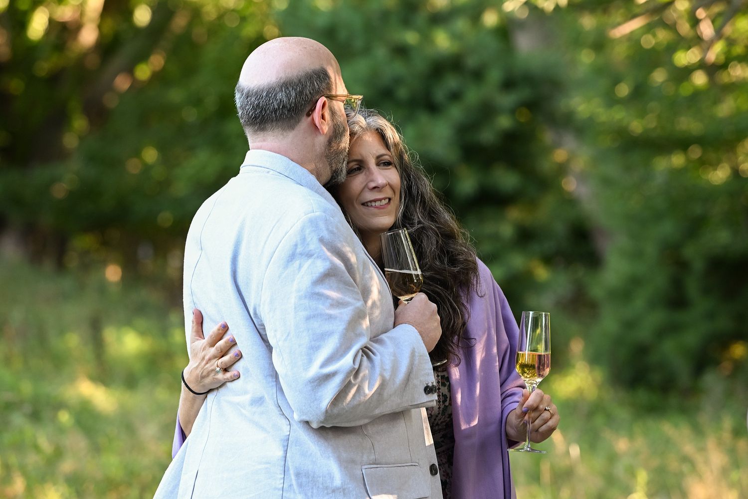 A couple shares a romantic moment in a sunlit garden setting with lush green foliage in the background.