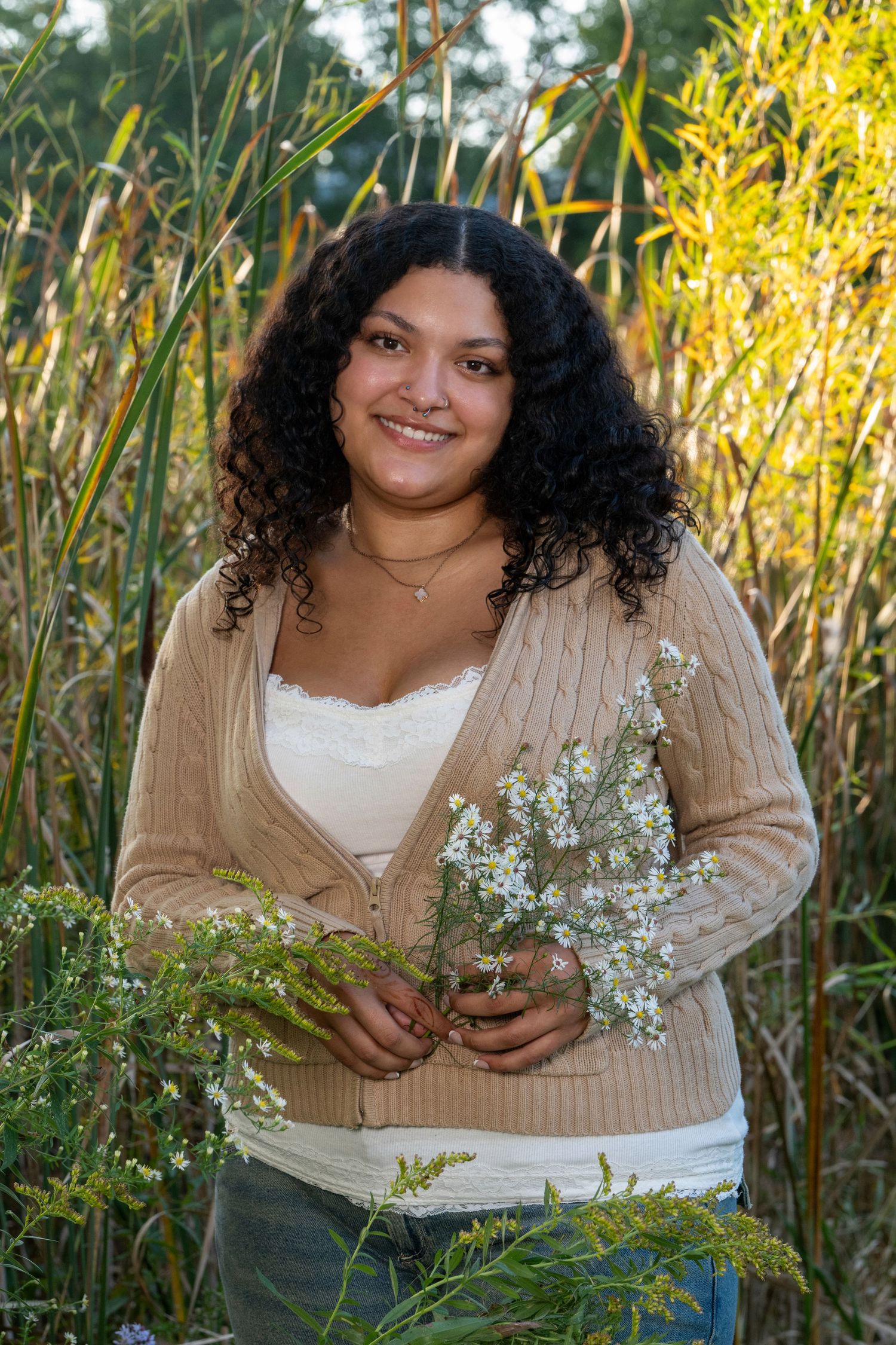 Person in a beige cardigan poses with delicate white flowers against tall grass.