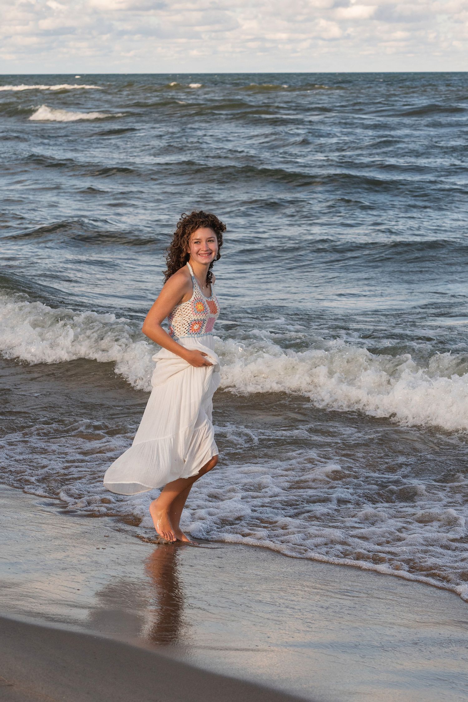 Someone in a white summer dress splashes playfully in the beach surf.