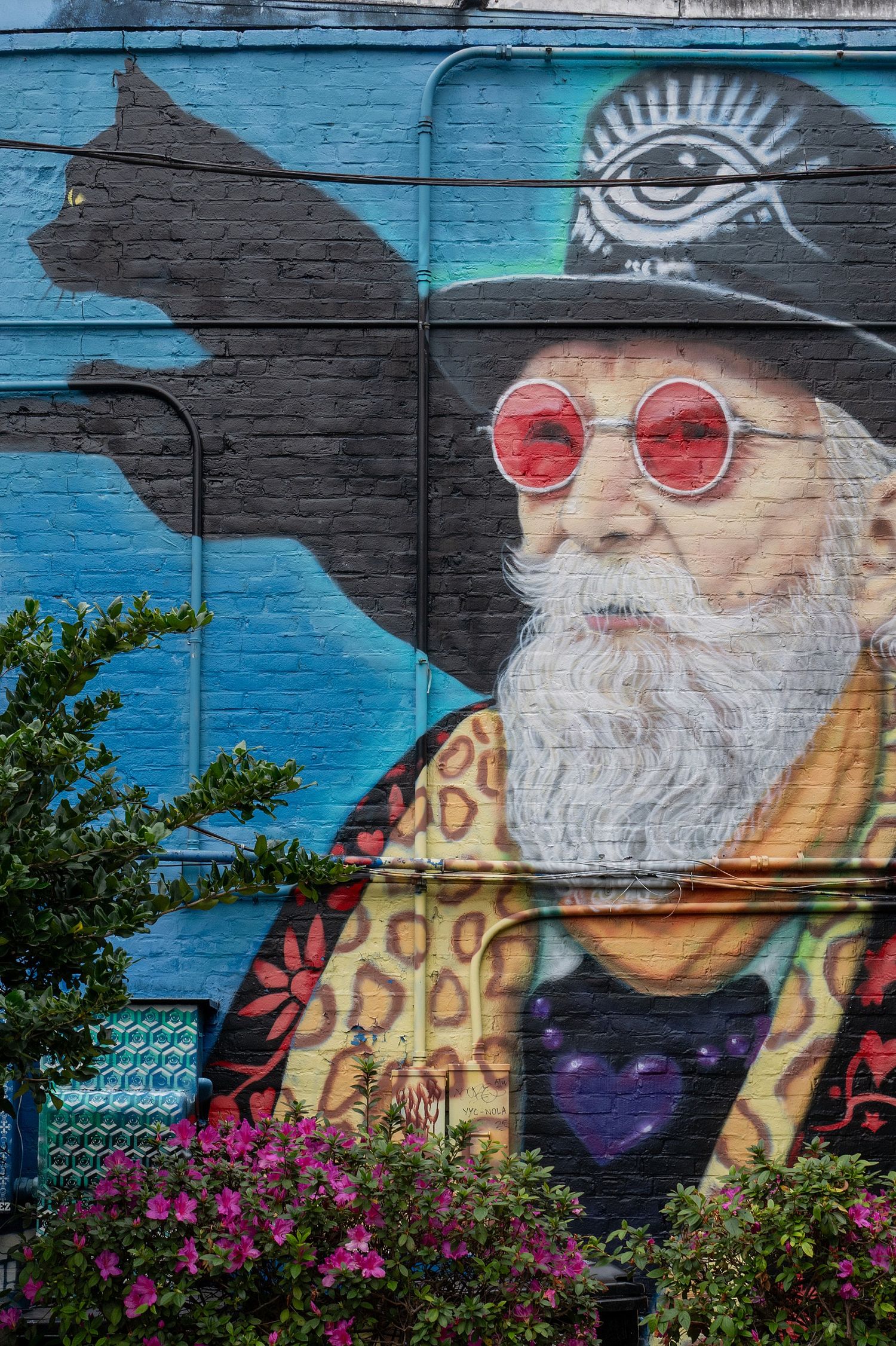 Colorful street art mural on brick wall featuring musician with sunglasses and white beard against blue background.
