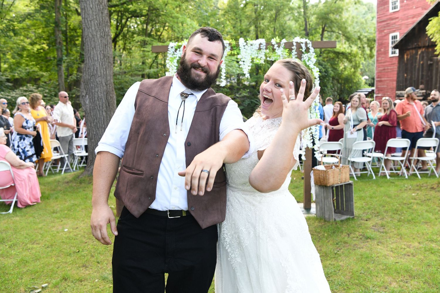 Casual outdoor wedding reception with rustic decor and string lights in wooded setting.