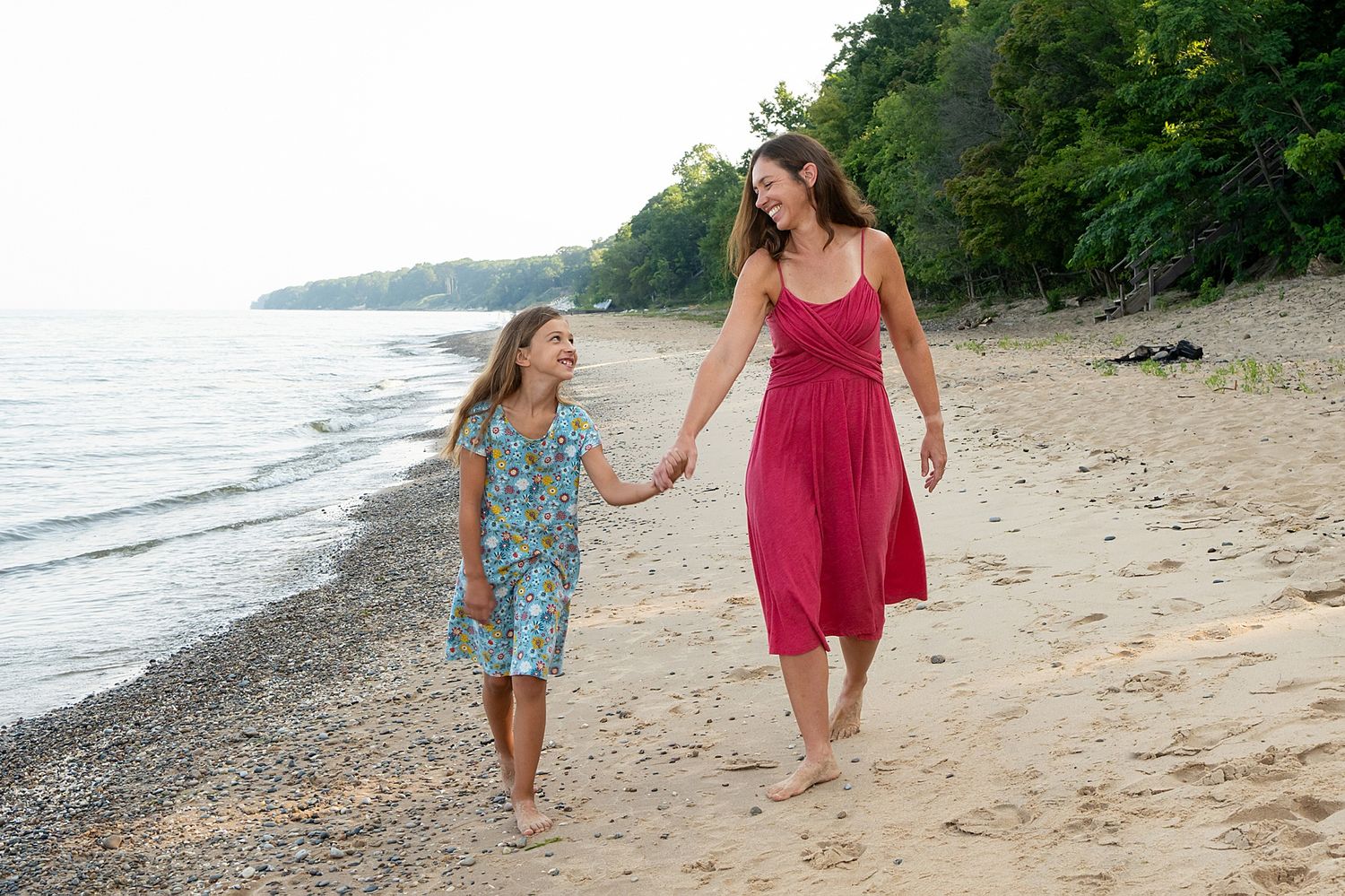 Mother and child walking along scenic beach shoreline at sunset.