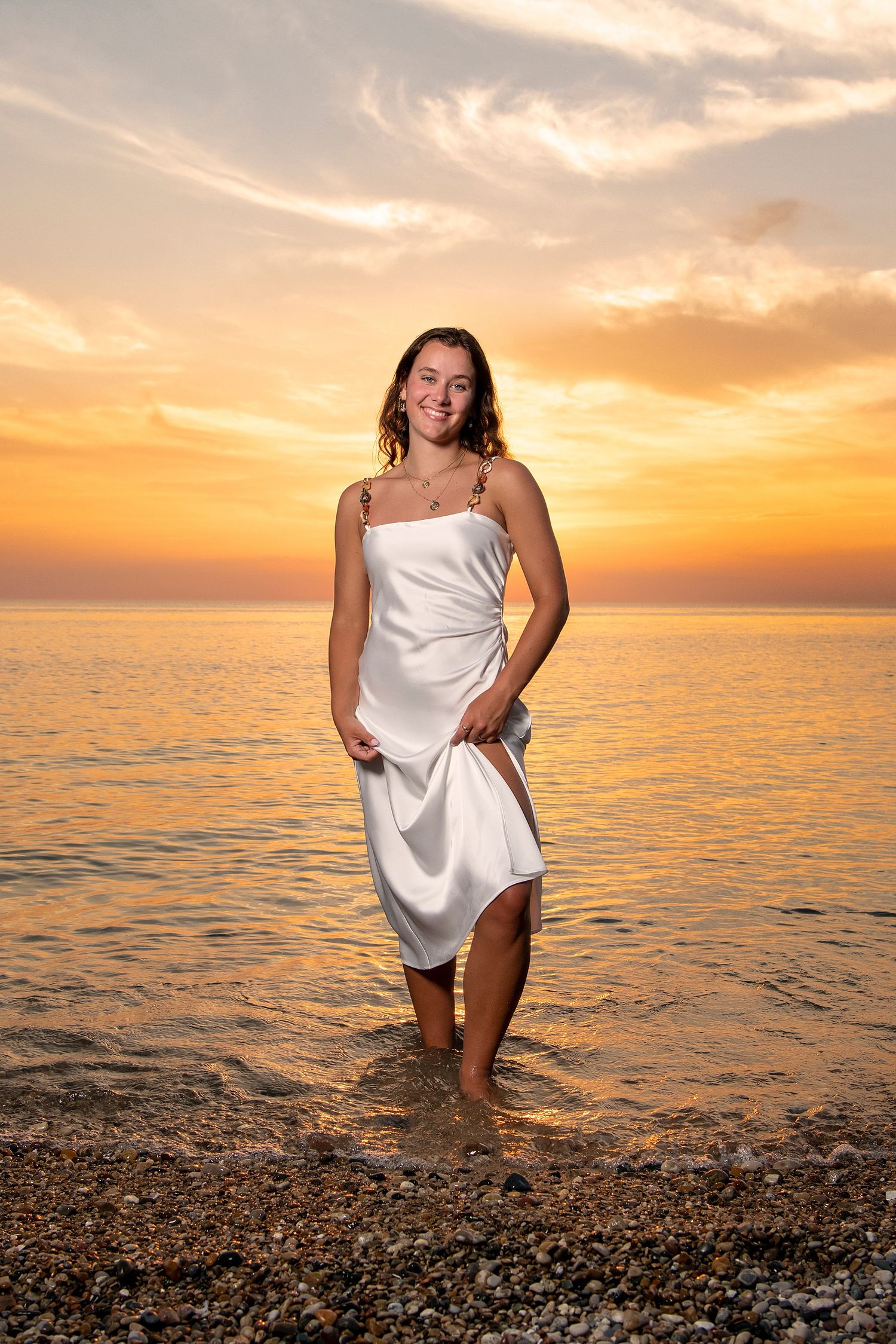 Person in white dress poses at beach during golden sunset.