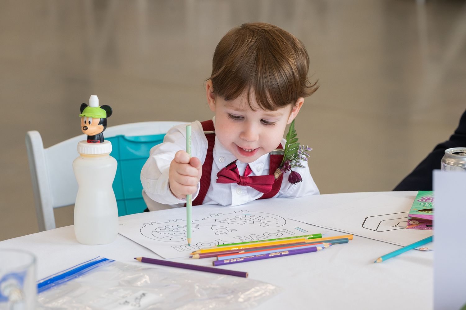 Young boy in bow tie colors at wedding reception table with pencils.