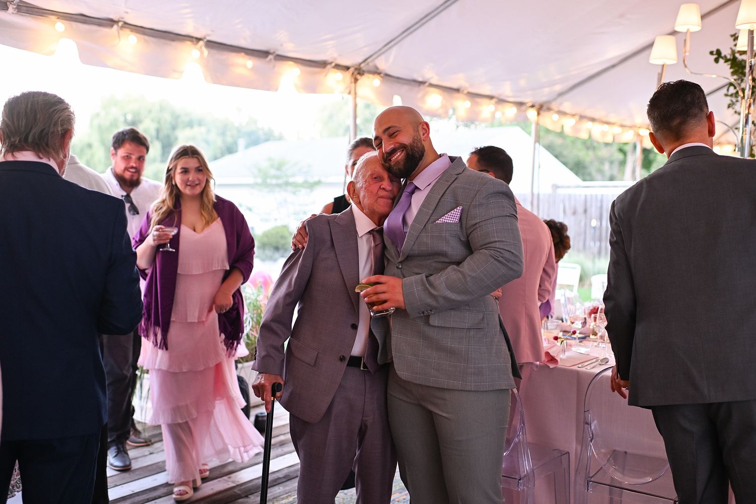 Wedding guests socialize and celebrate under a white tent at an outdoor reception.