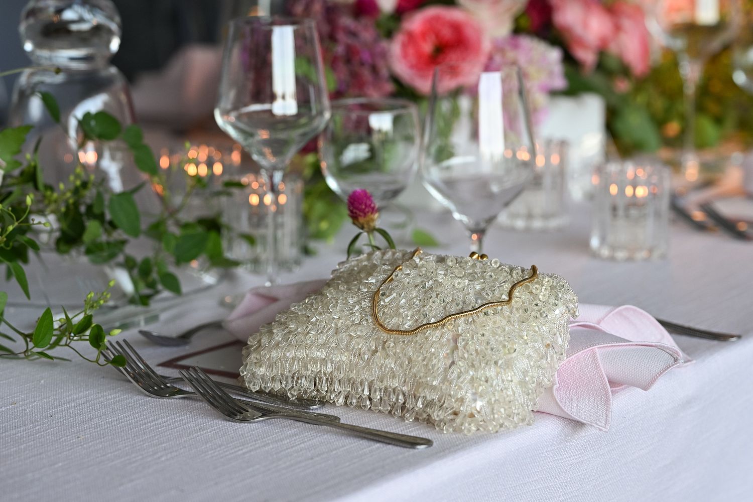 Elegant table settings at a wedding reception with pink floral centerpieces and crystal glassware on white linens.