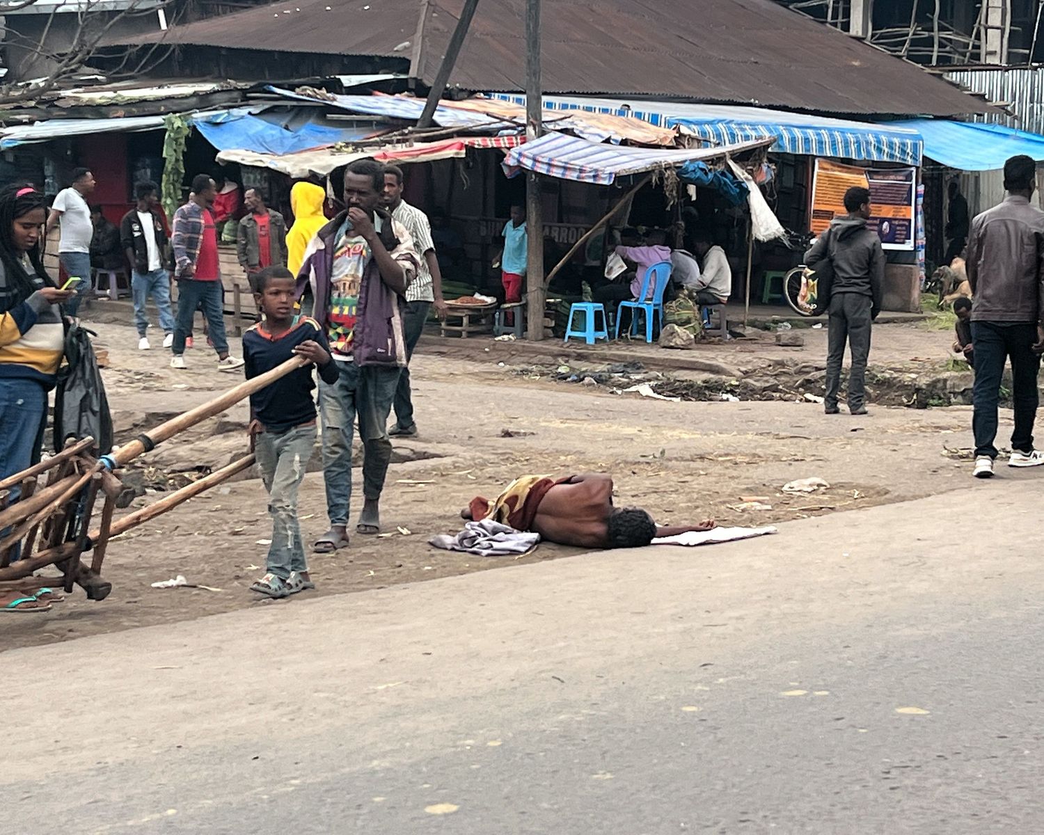 Busy street scene with market stalls and people walking along a dirt road.