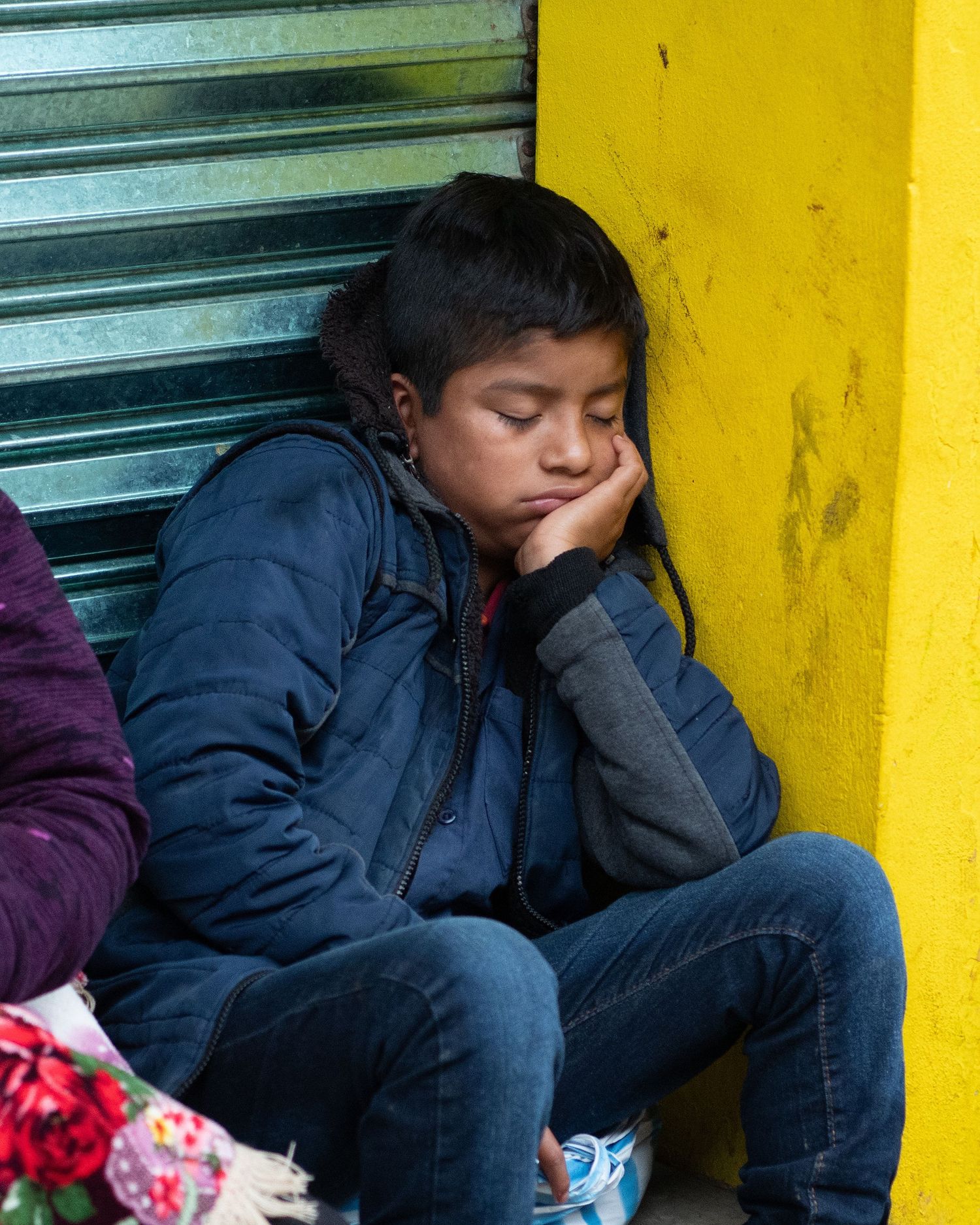 Person in navy jacket sitting against yellow wall.