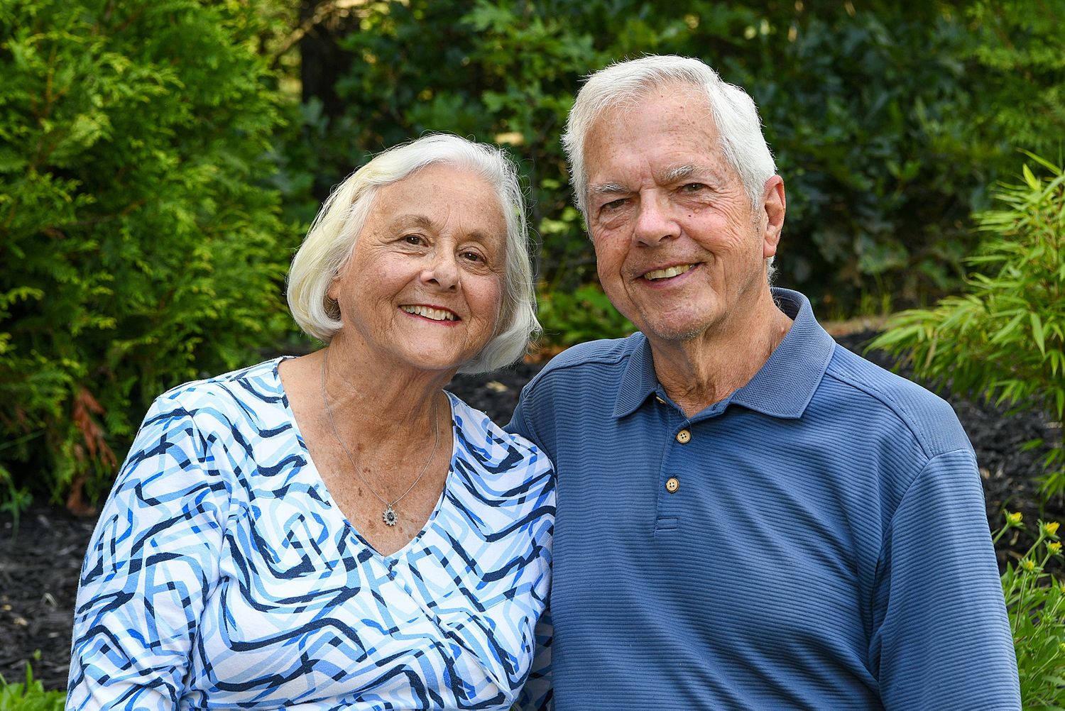 Couple enjoying a tender moment together in a garden setting with green foliage background.
