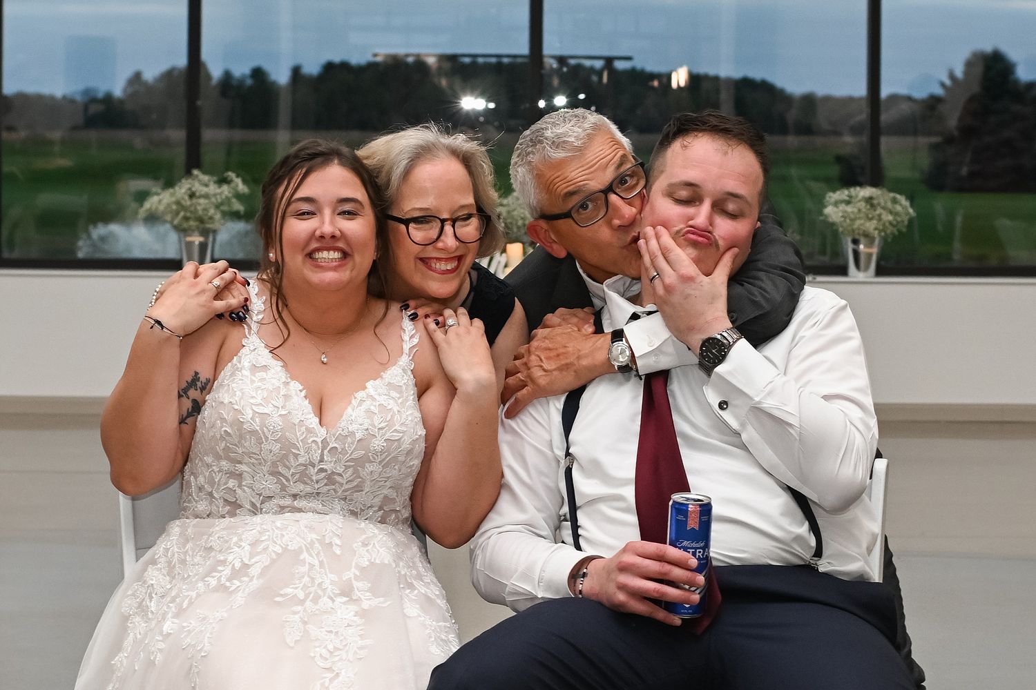 Bride and groom posing with parents for fun wedding reception photo, laughing and smiling together.