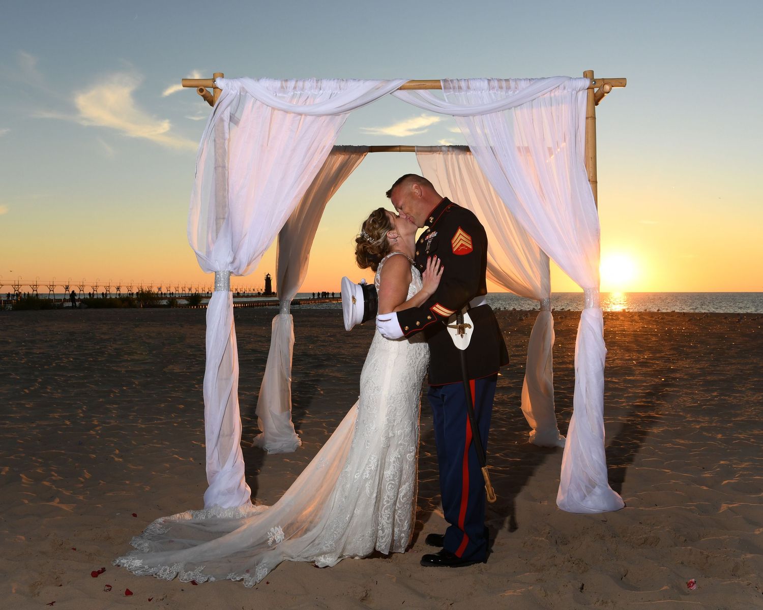 Beach wedding ceremony setup with white fabric canopy at sunset.