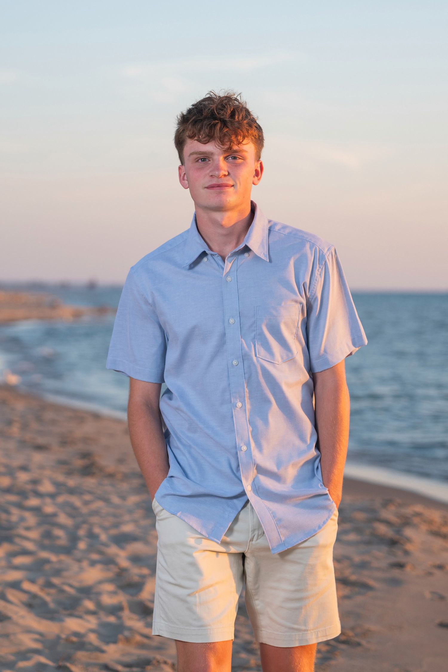 Person in casual summer attire poses on sandy beach with ocean in background.