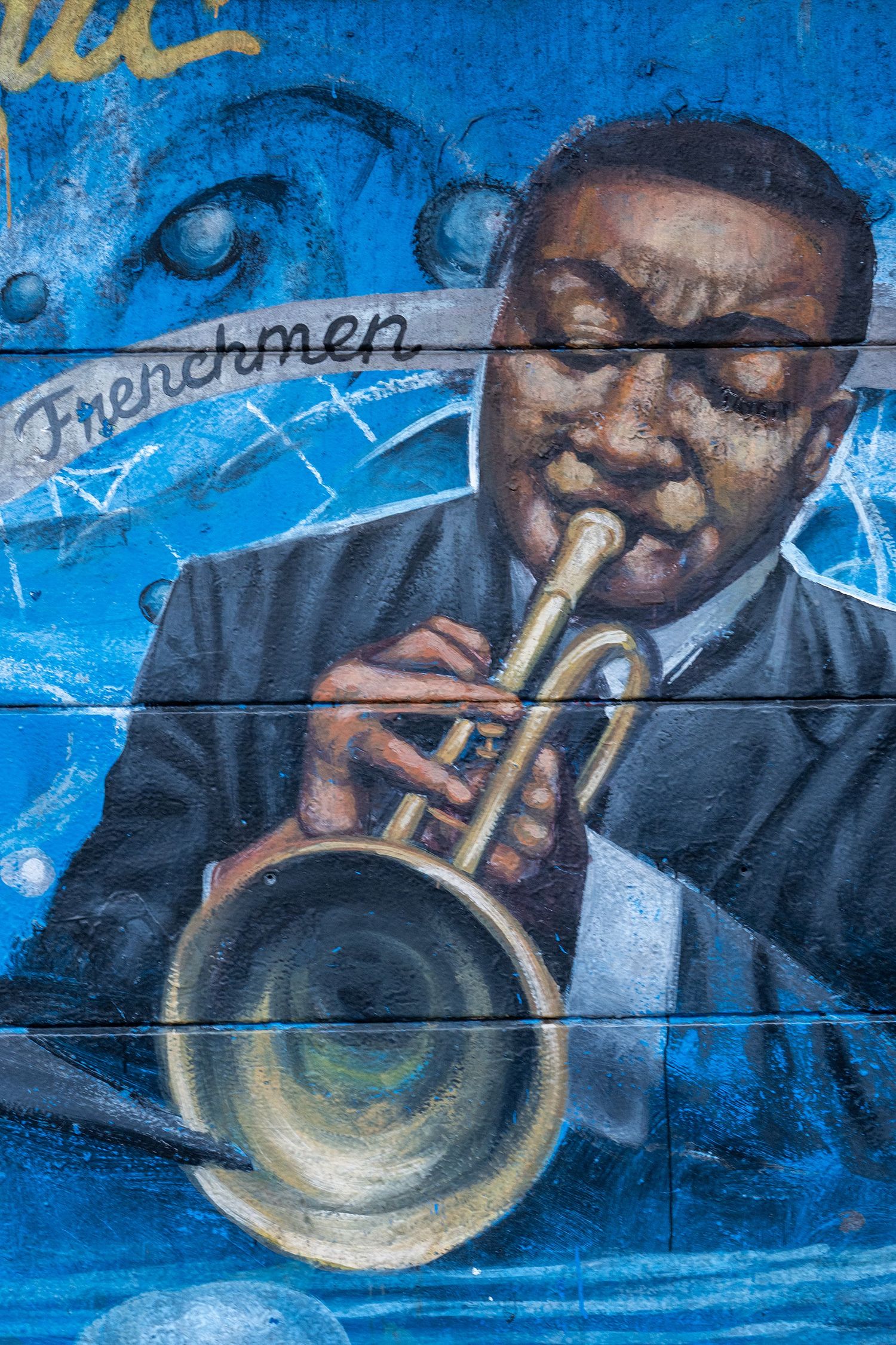Vibrant blue street art mural depicting a trumpet player performing jazz music against a deep blue background.