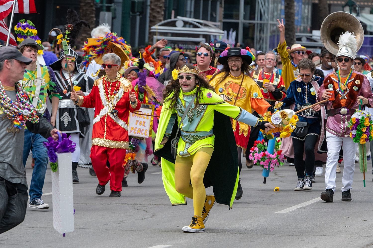 Festive Mardi Gras parade participants in vibrant costumes marching down a crowded street.