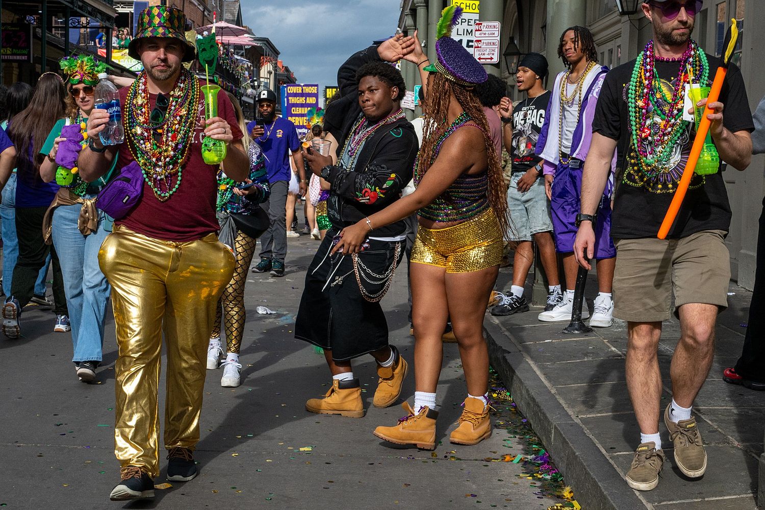 Colorfully dressed festival goers celebrate on a city street during Mardi Gras with beads and costumes.