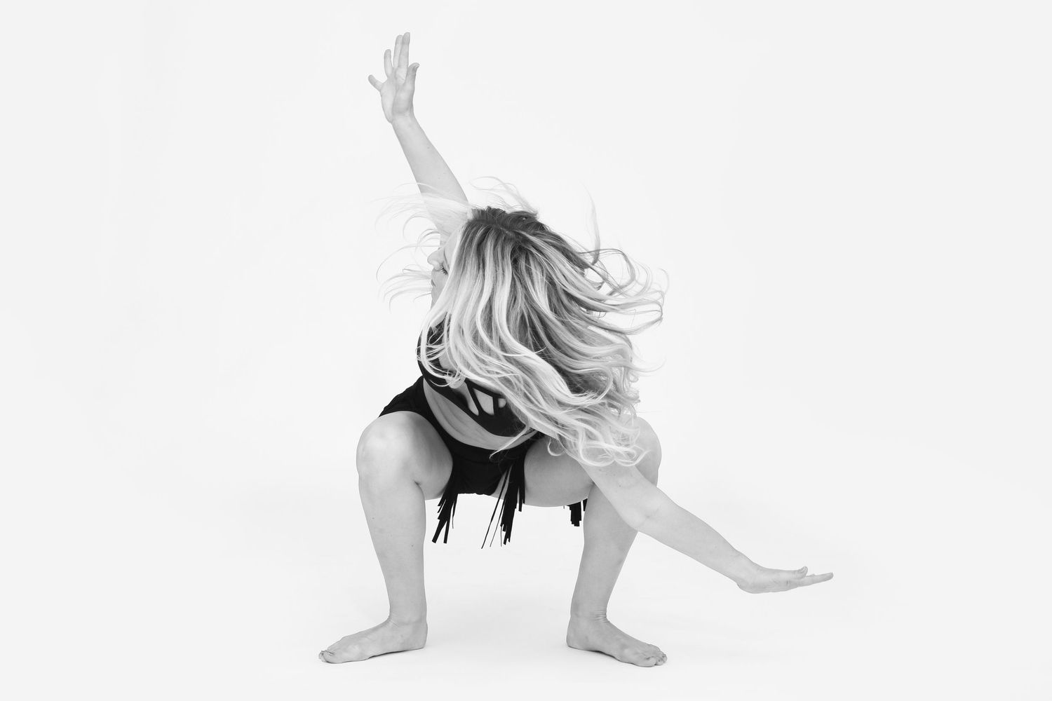 Contemporary dancer stretching and posing in black outfit against white backdrop.