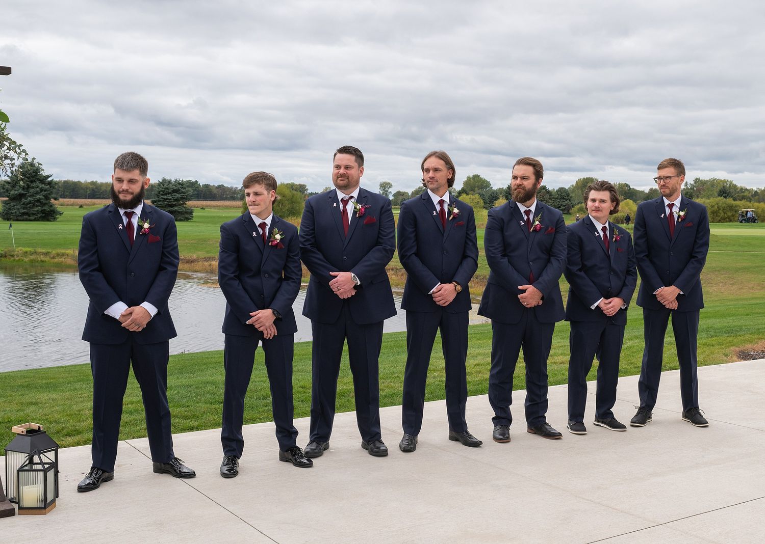 Seven groomsmen in matching navy suits posing together outdoors at golf course wedding venue.